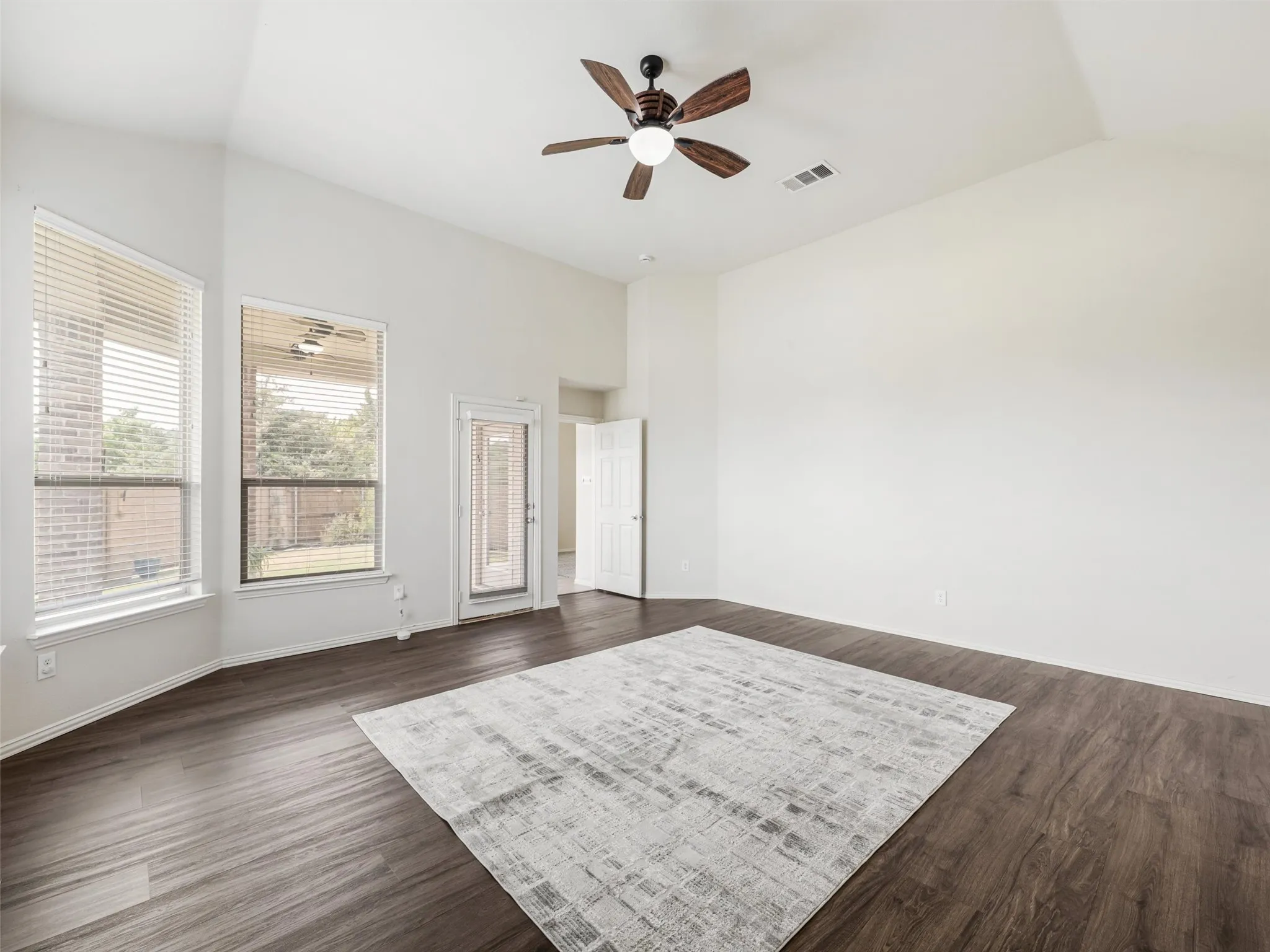 Expansive primary bedroom features vaulted ceilings, laminate flooring, a ceiling fan, and direct access to the ensuite bathroom as well as outdoor patio.