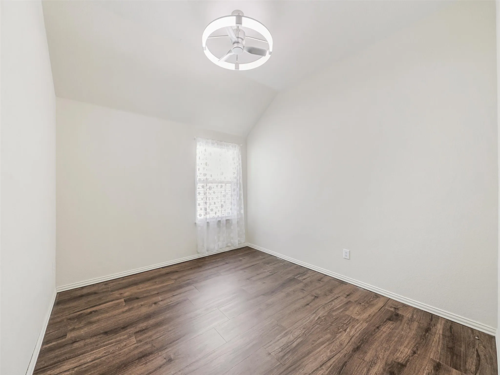 Bright secondary bedroom features a vaulted ceiling, modern ceiling fan, wood-look flooring, and a window for natural light.