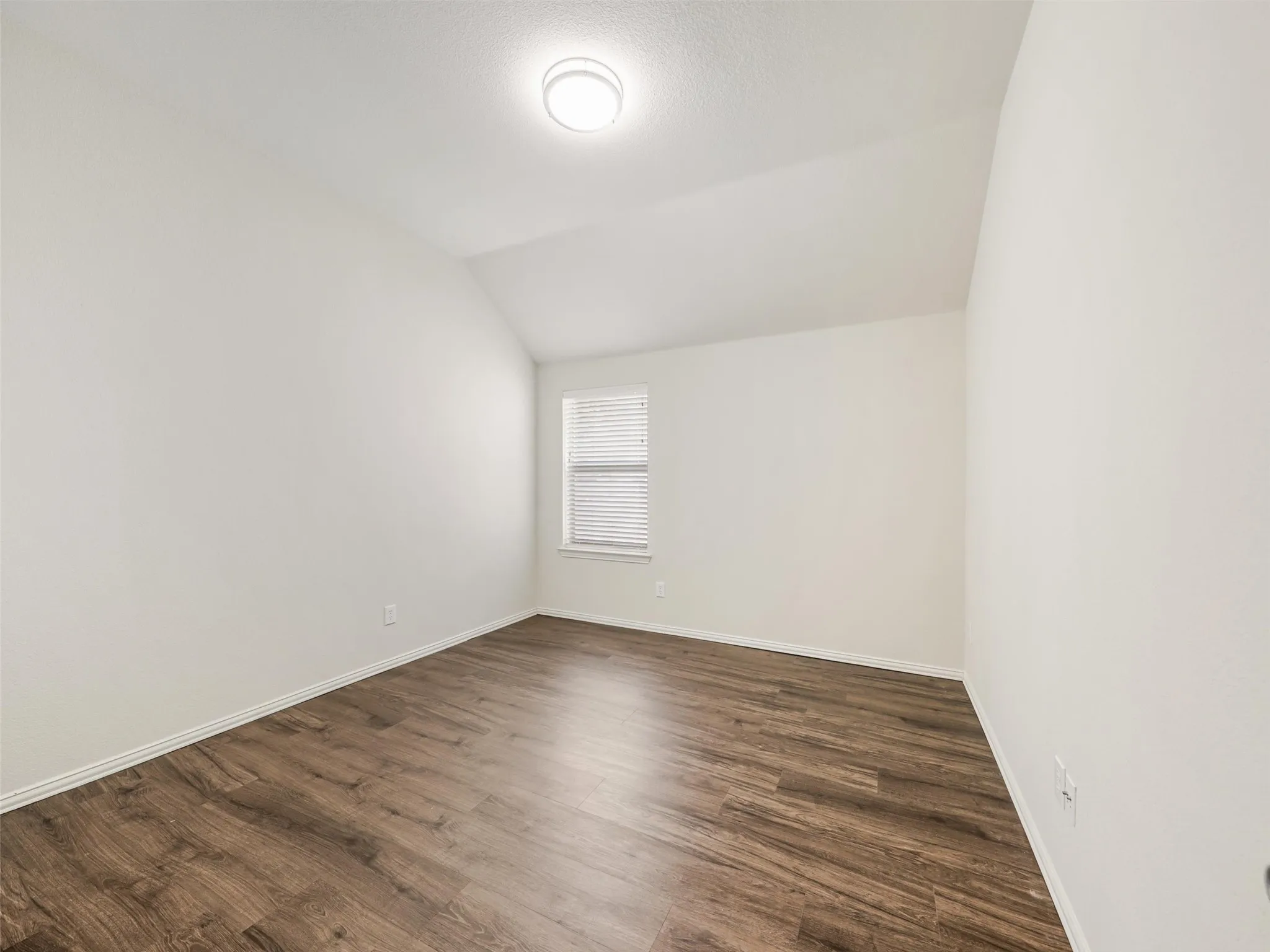 Another spacious secondary bedroom with a vaulted ceiling, neutral finishes, wood-look flooring, and abundant natural light.