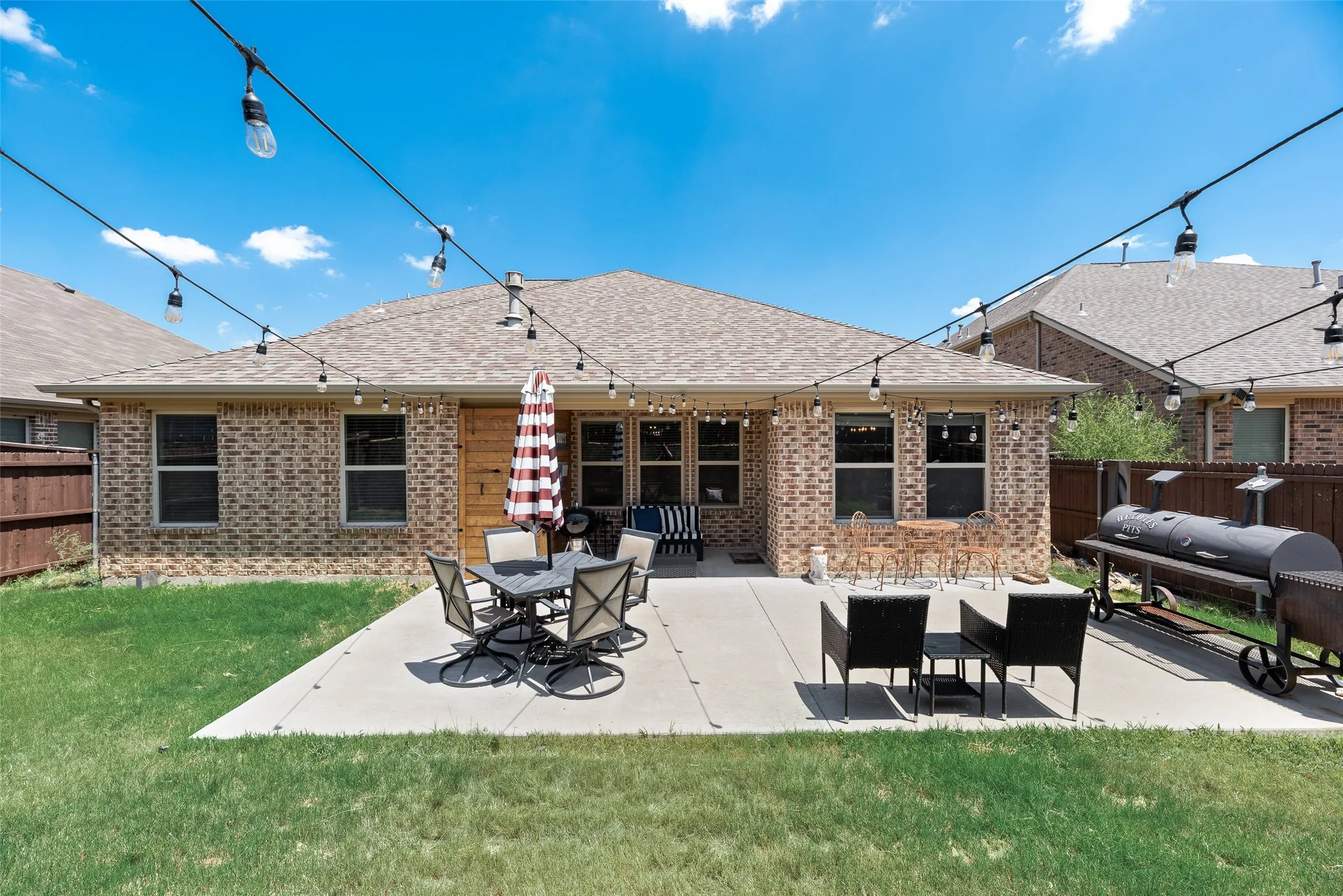 Spacious concrete patio with string lights, brick exterior, and a wood-paneled door