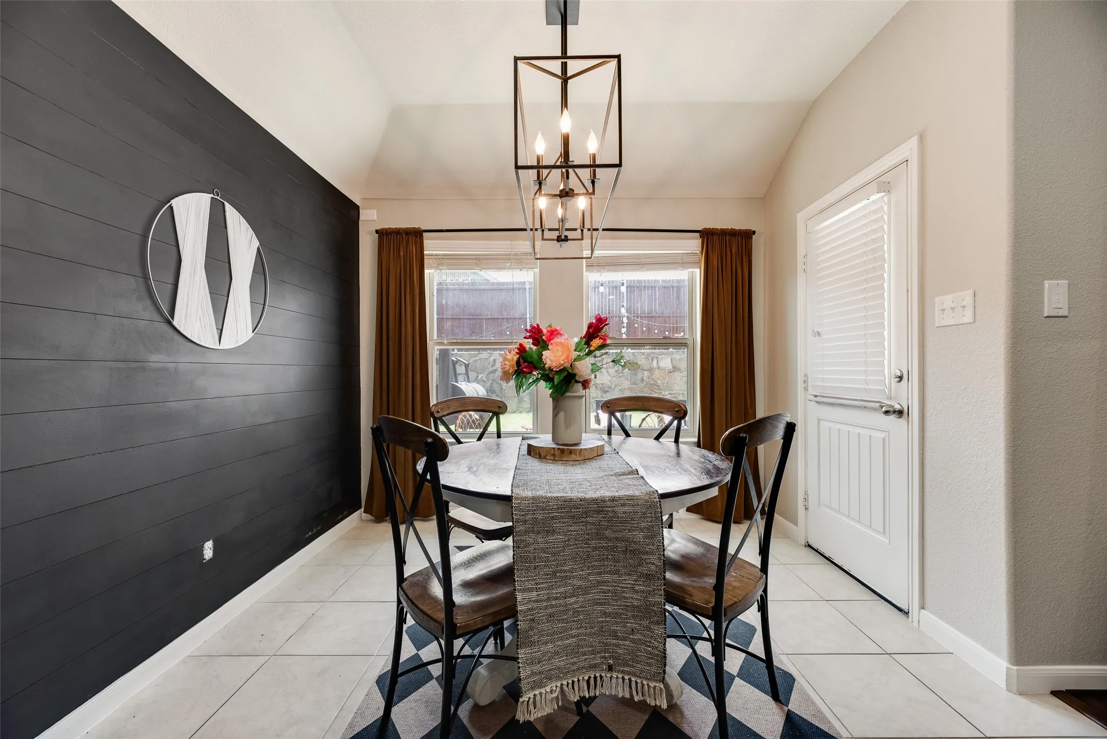 Vaulted ceiling with an open-cage chandelier, shiplap accent wall, tile flooring, and a window with blinds