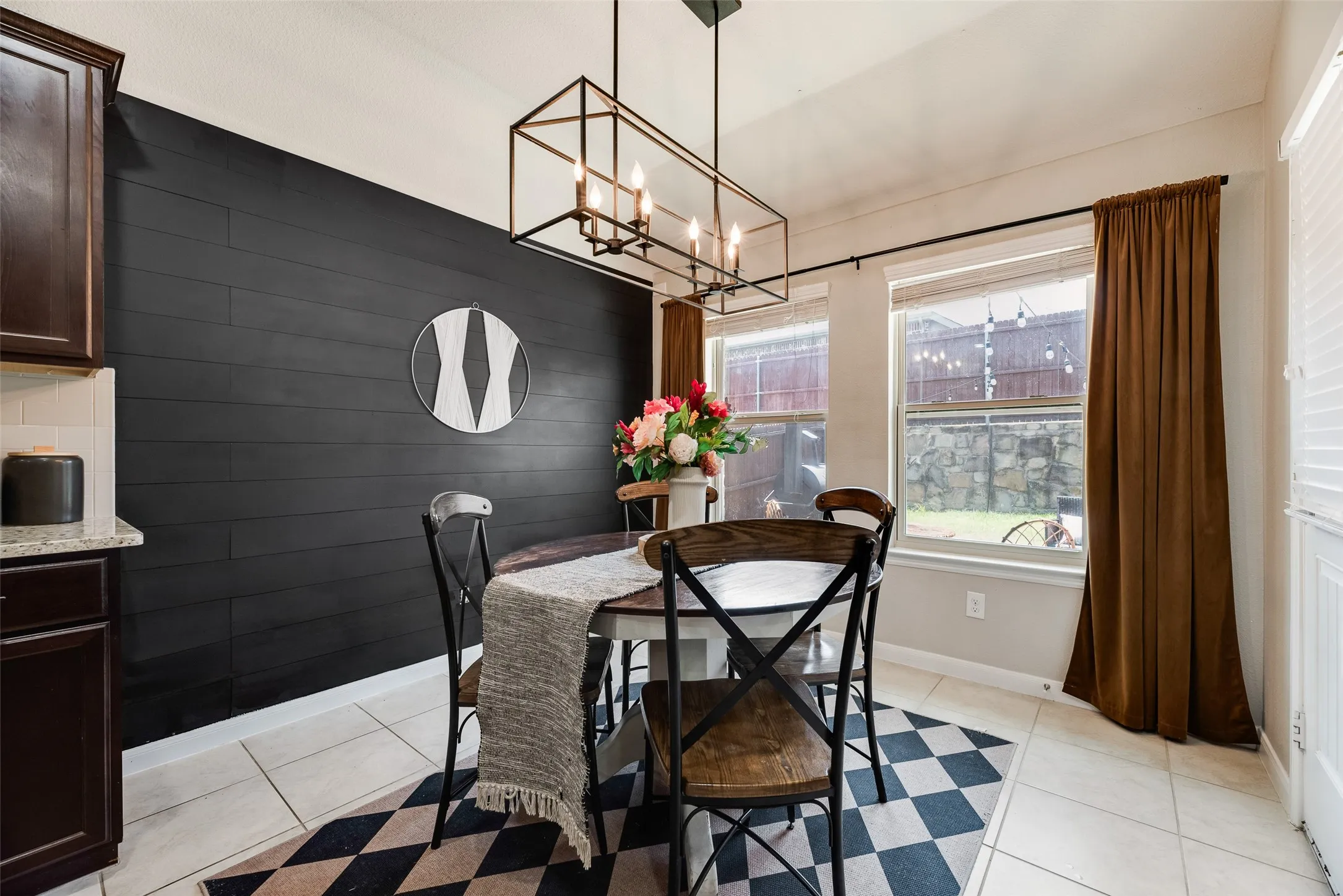 Black shiplap accent wall, contemporary linear chandelier, tiled flooring, built-in cabinetry, and double windows with roller shades