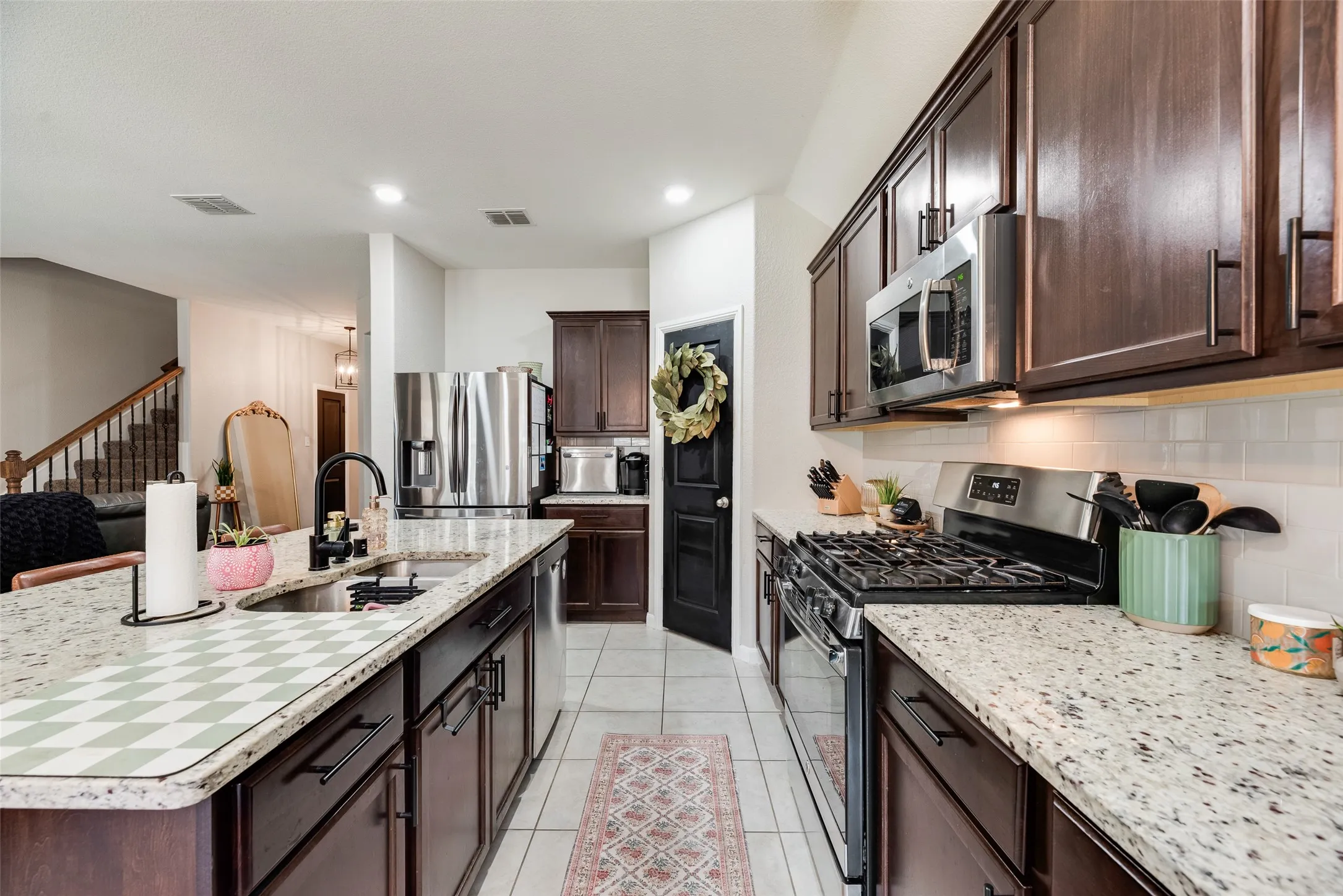Kitchen featuring dark wood-finish cabinetry, stainless steel appliances, speckled stone countertops, and a tile backsplash