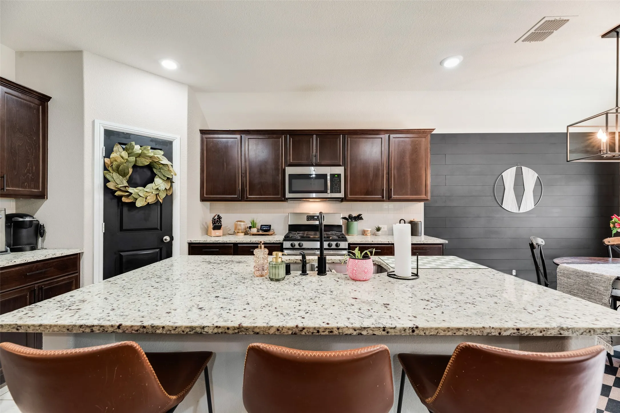Expansive kitchen island with a light-toned countertop, dark wood-finish cabinetry, stainless steel appliances, recessed lighting, and a linear pendant light fixture