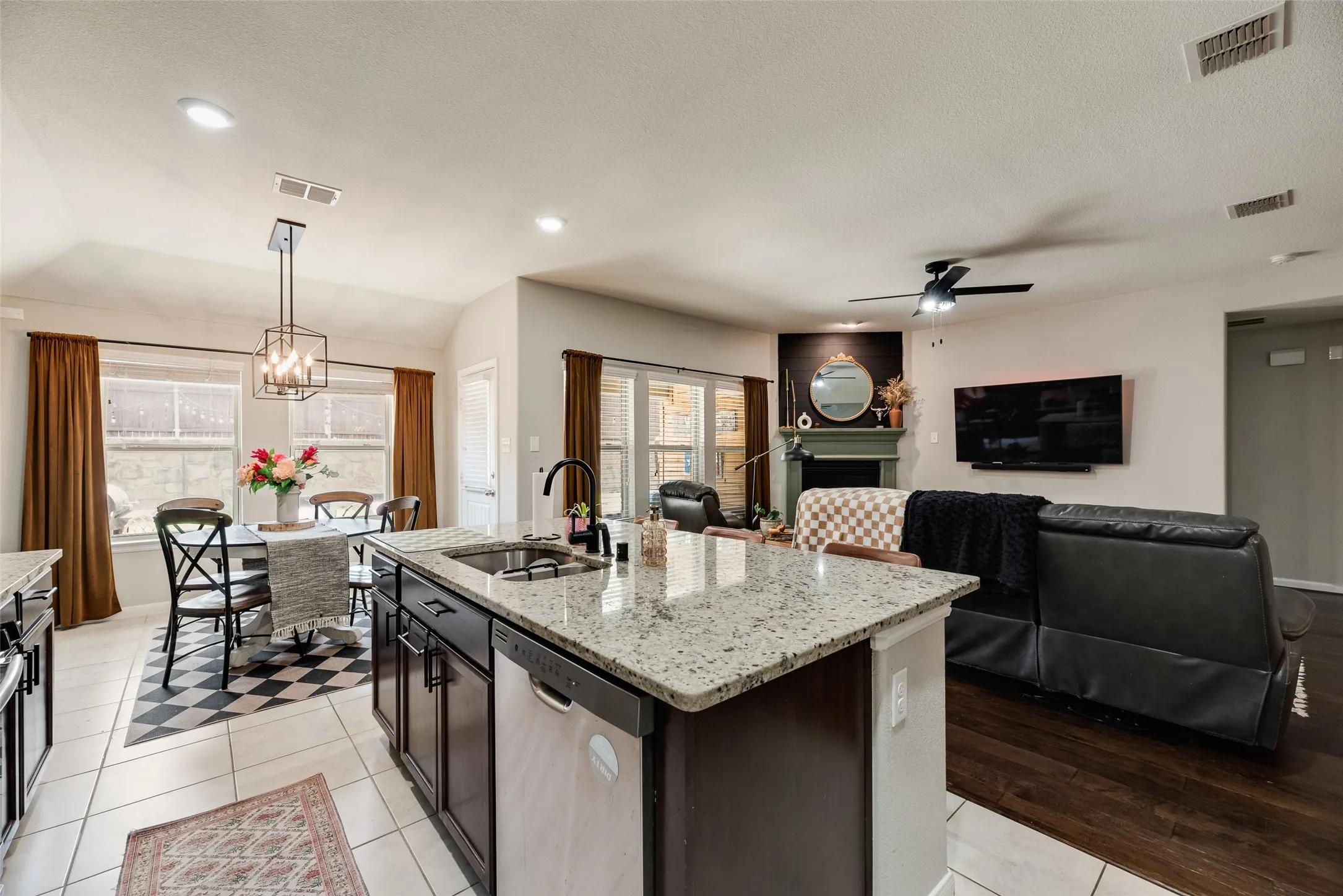 Kitchen island with granite countertop and undermount sink, dark wood-finish cabinetry, tile flooring, and recessed lighting
