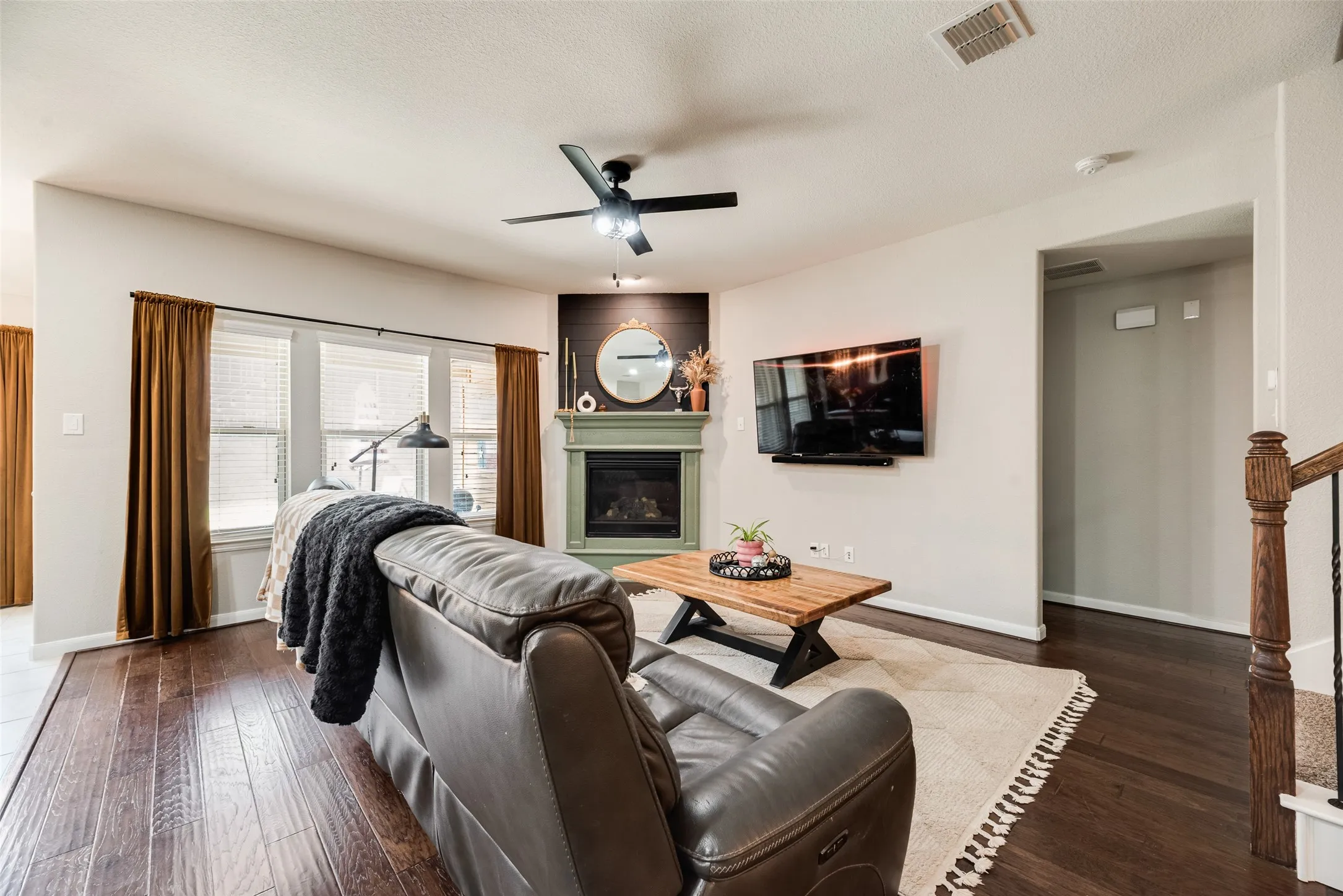Fireplace with mantle, wood-finish flooring, ceiling fan, and staircase with wood newel post and metal balusters