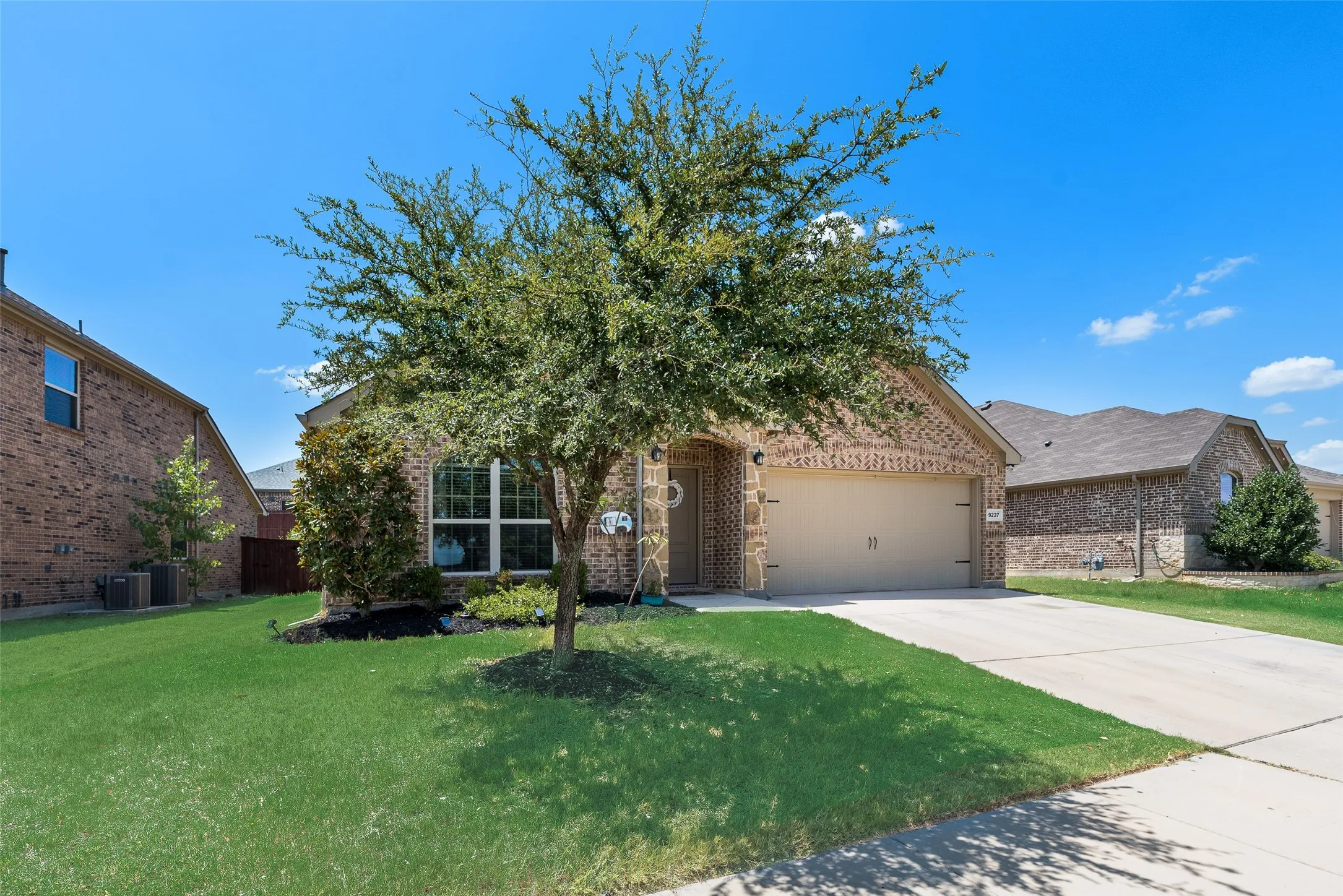 Brick exterior with an attached garage, landscaped front yard, and a concrete driveway