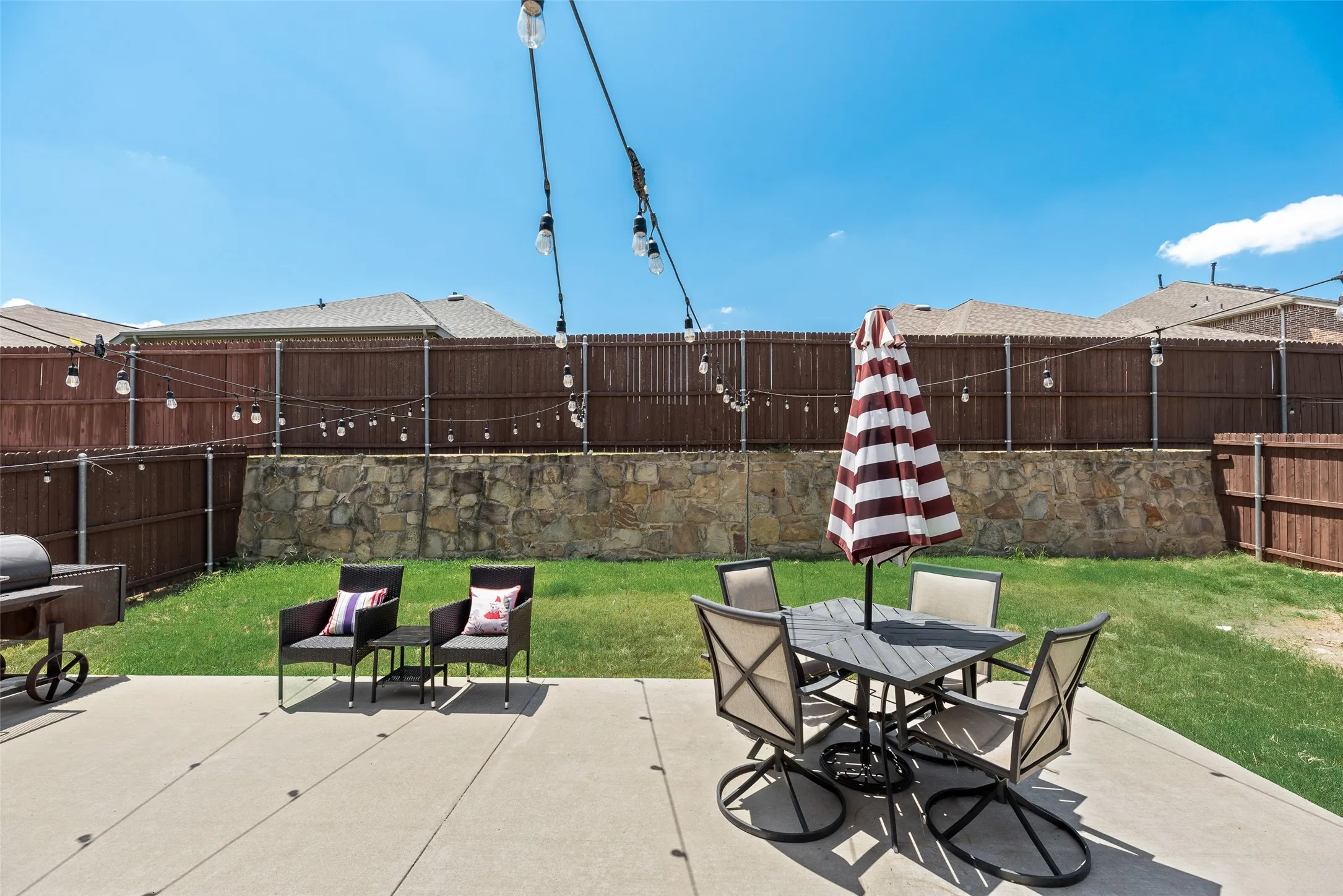 Expansive concrete patio with string lighting, stone retaining wall, and wood fencing