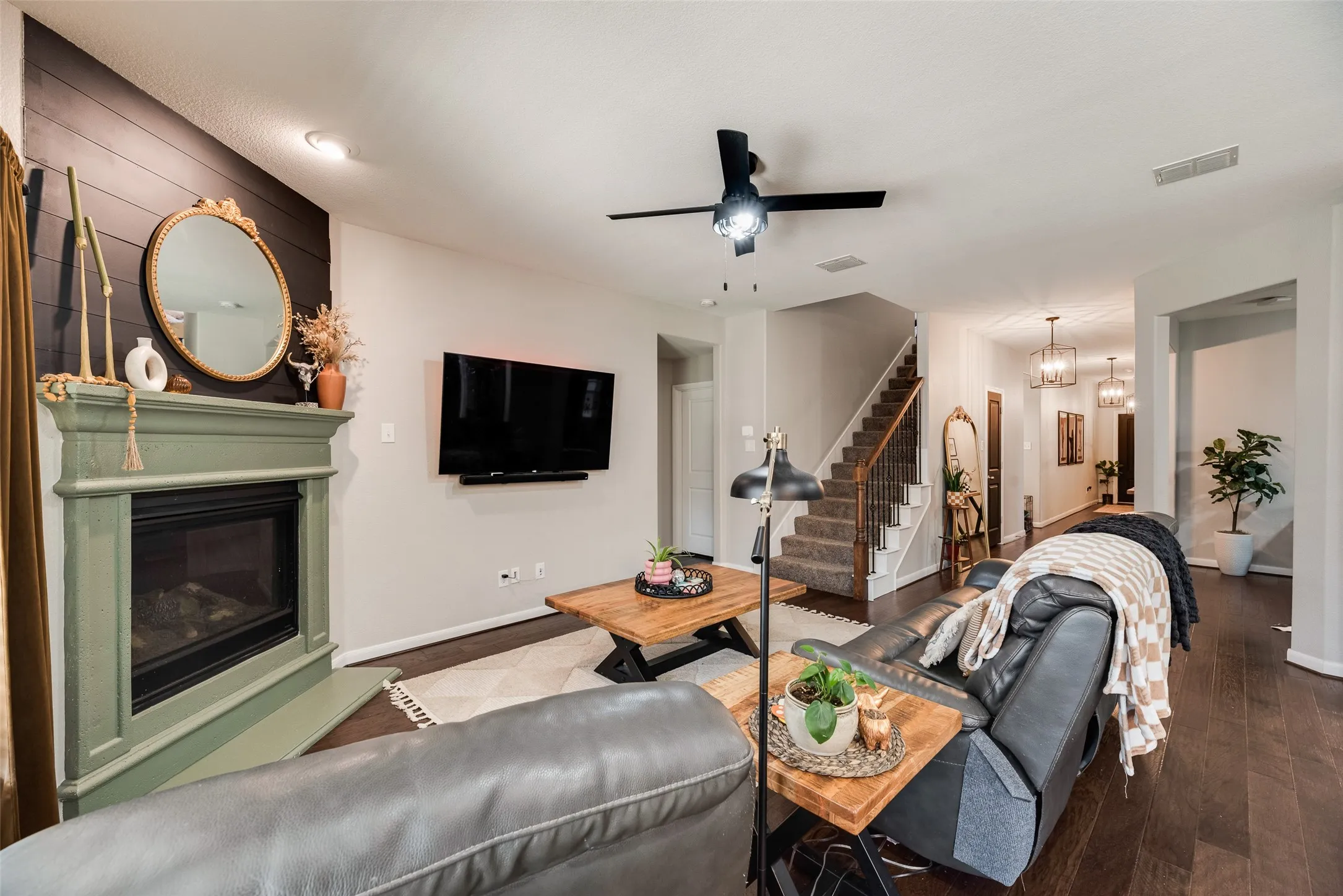 Living area featuring a fireplace with a painted mantel, dark wood-finish flooring, a ceiling fan, and a staircase with wrought iron balusters