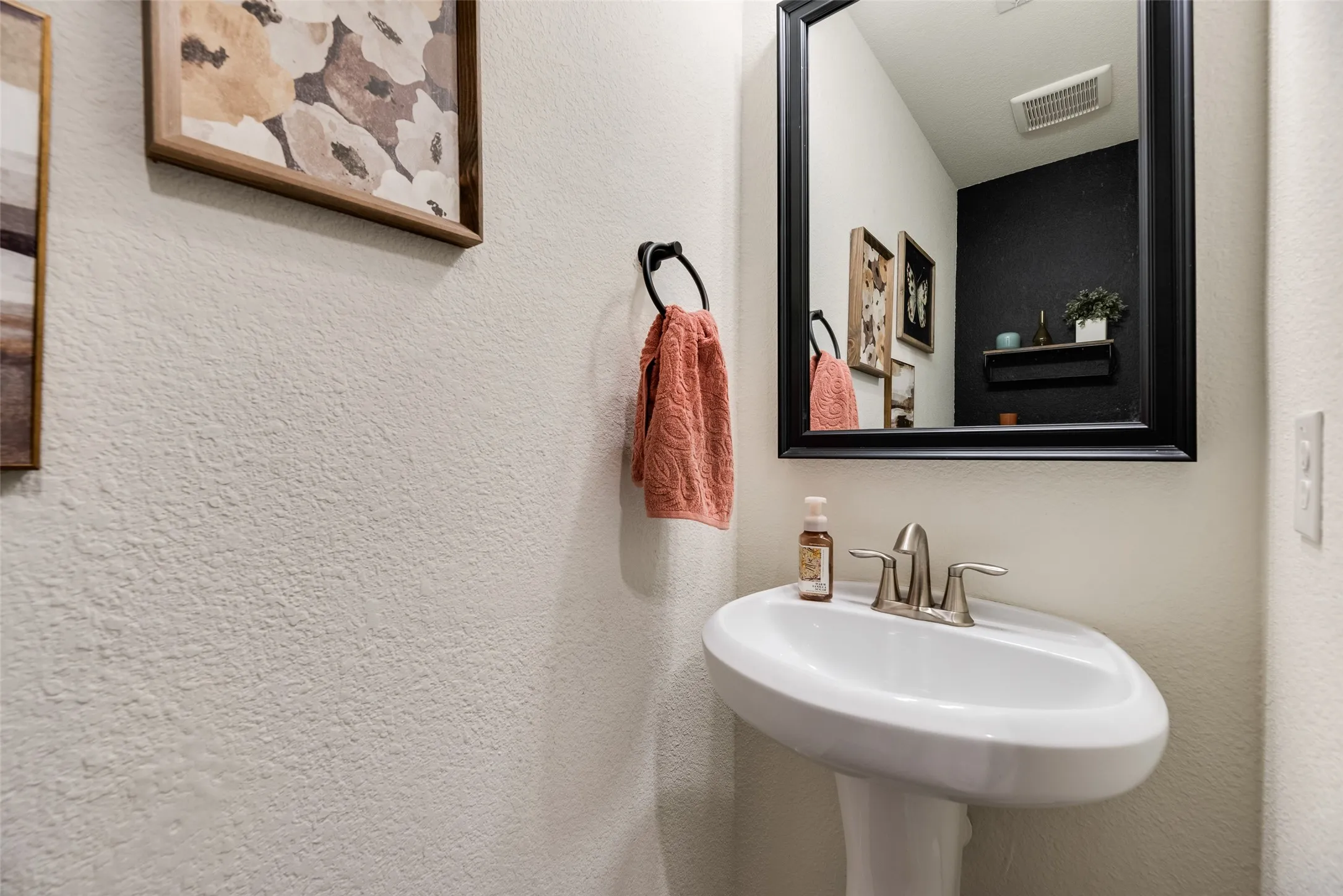 Pedestal sink with a brushed nickel faucet and a framed mirror