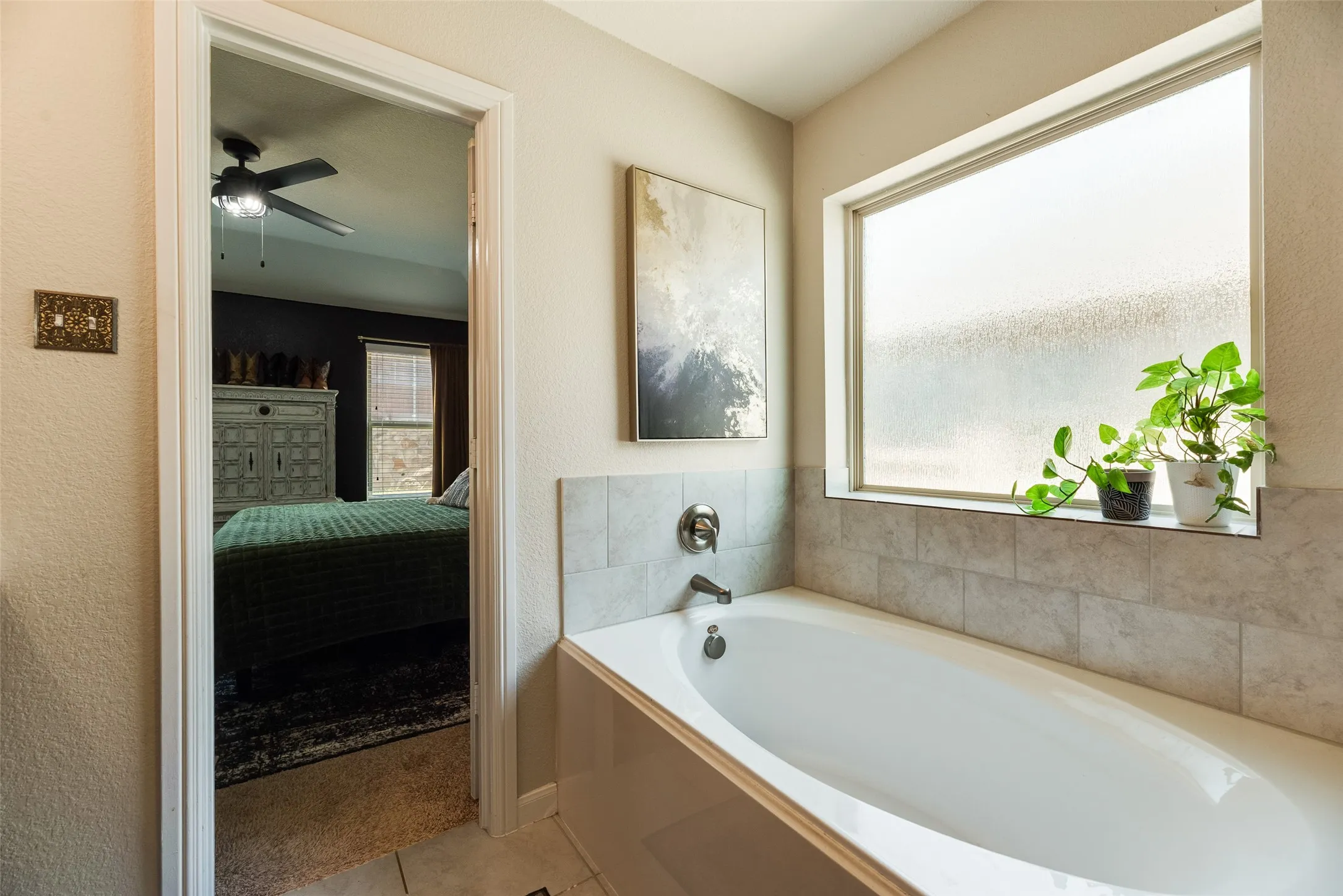 Soaking tub with tile surround, frosted window, and wall-mounted faucet