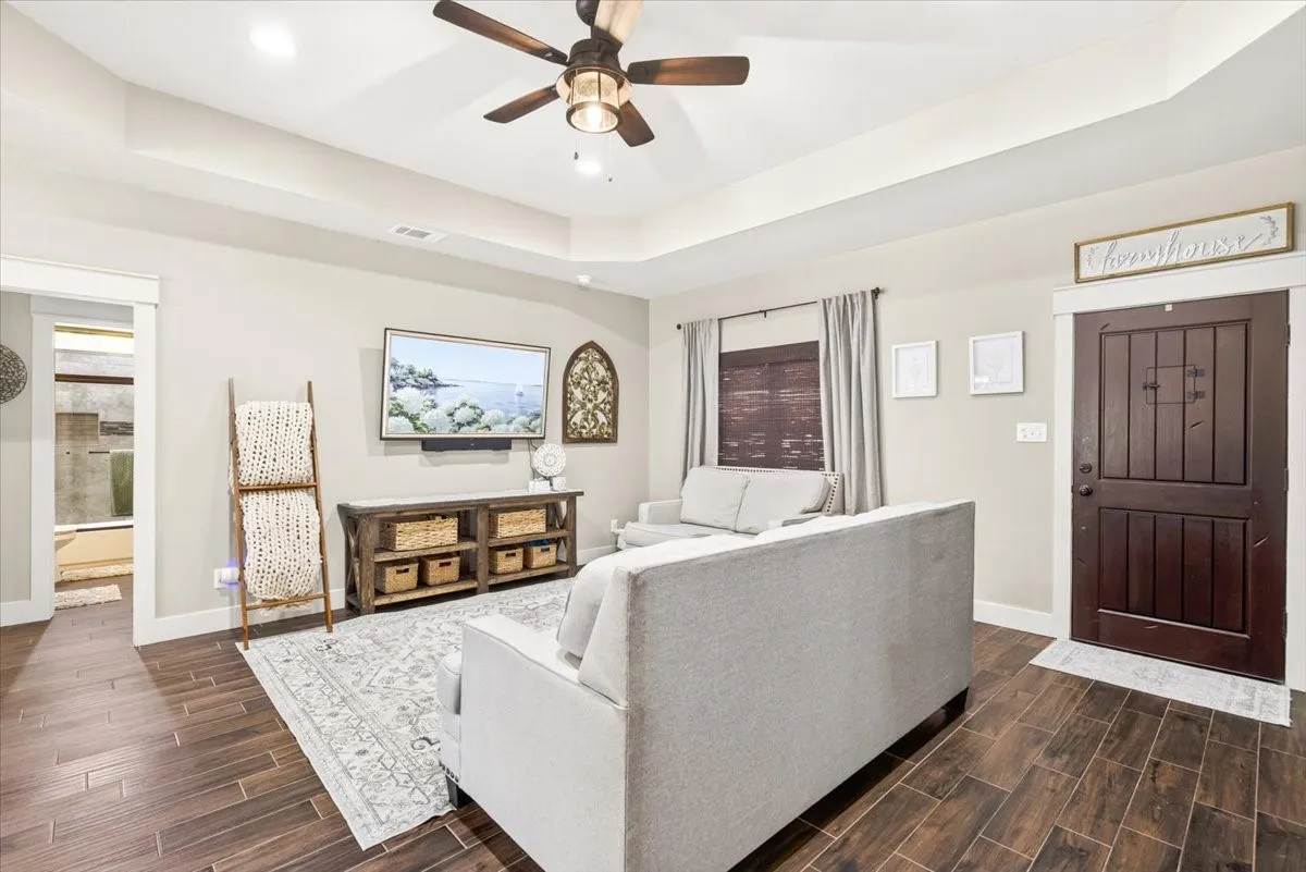 Tray ceiling with recessed lighting and a ceiling fan, wood-finish flooring, and a dark wood paneled entry door