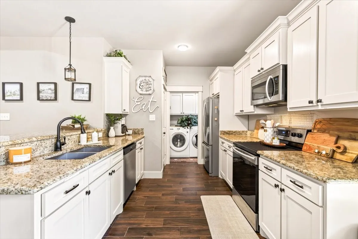 White cabinetry, wood-finish flooring, granite countertops, stainless steel appliances, and a built-in laundry area