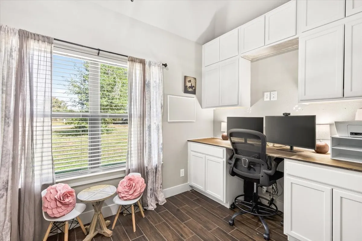 Built-in desk with wood-finish countertop, white cabinetry with under-cabinet lighting, and wood-look flooring