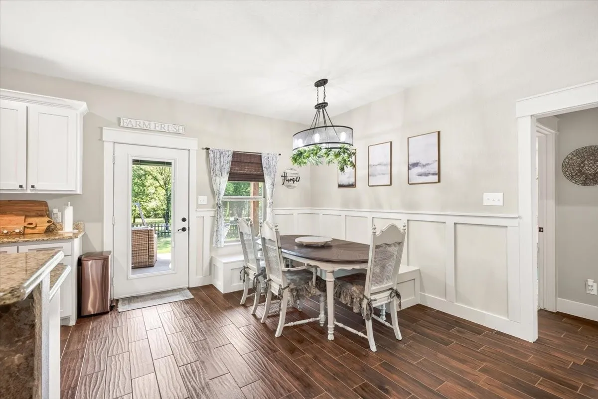 Wood-finish flooring, white shaker cabinetry, granite-style countertops, white board and batten wall detailing, and a built-in bench