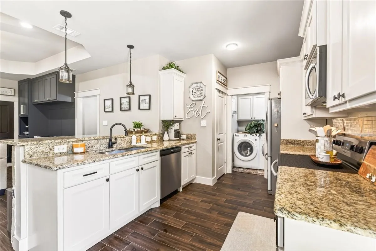 Kitchen featuring granite countertops, white cabinetry, stainless steel appliances, wood-finish flooring, and a dedicated laundry area