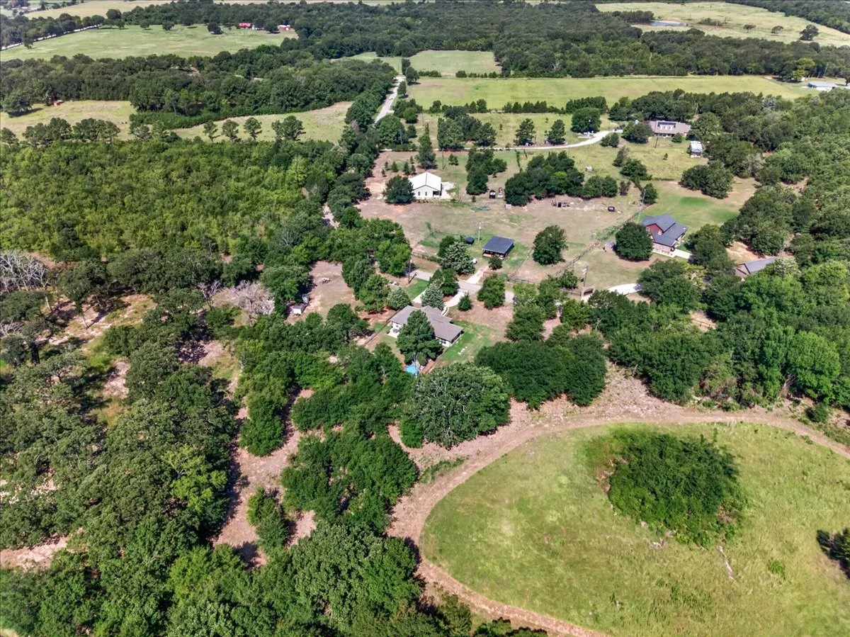 Expansive property featuring wooded areas, open grassy fields, multiple structures, and a winding unpaved road
