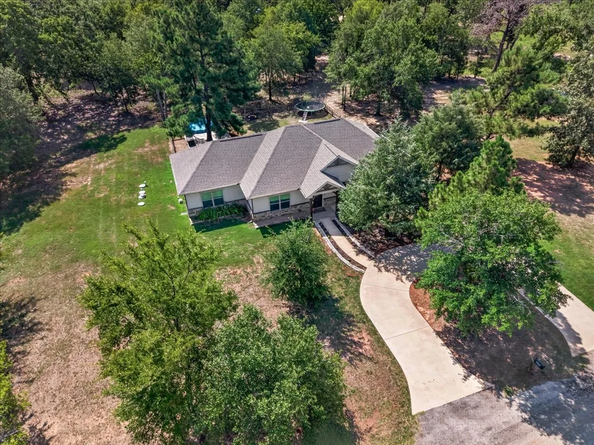 Single-story residence with a gray shingle roof, stone and siding exterior, and an expansive concrete driveway