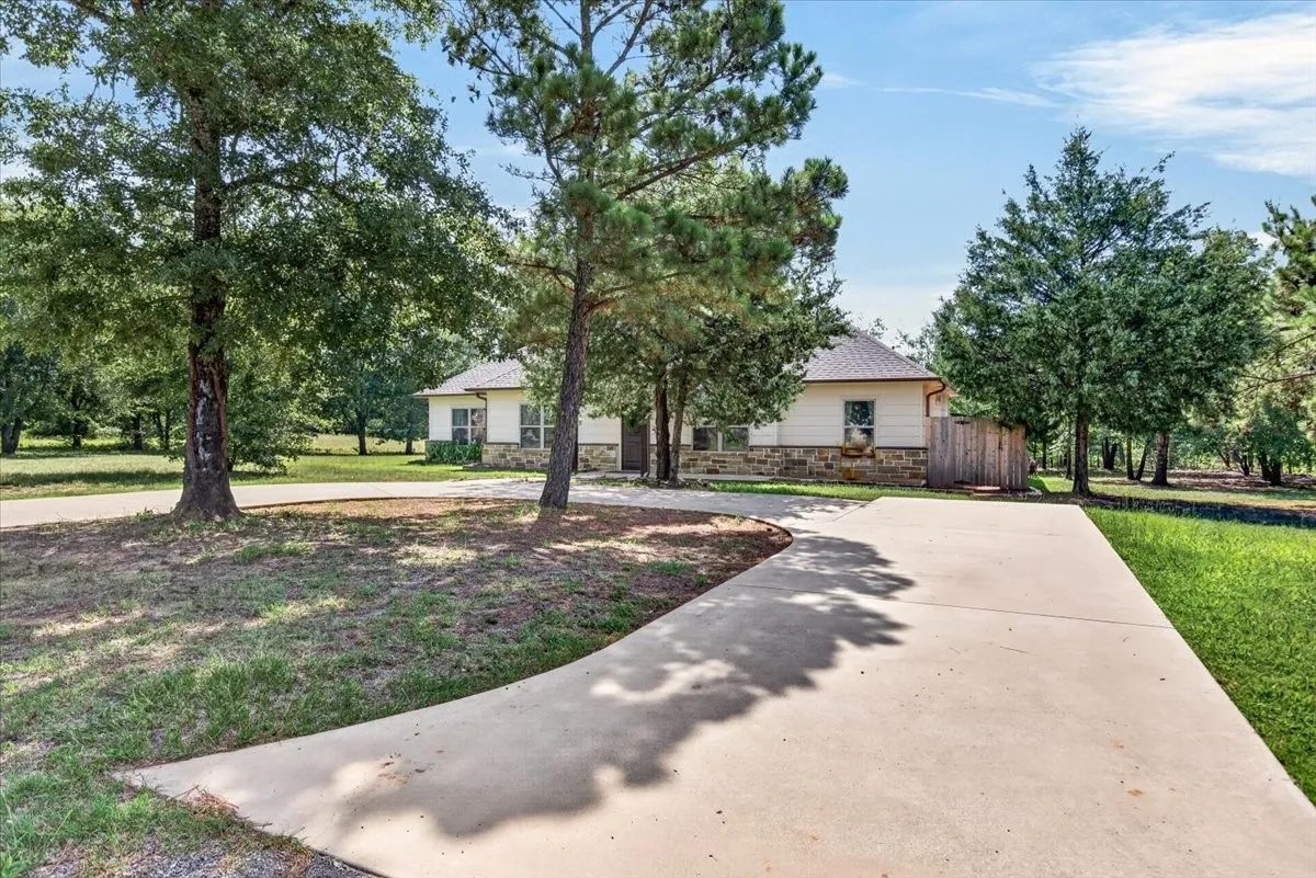 Exterior featuring a stone and siding facade, covered entrance, multiple mature trees, and a concrete circular driveway
