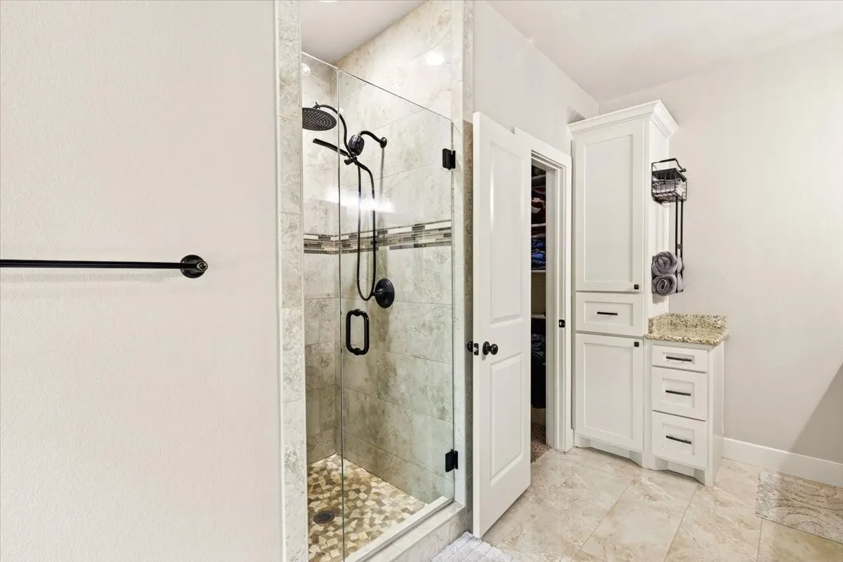 Glass-enclosed shower with pebble-finish flooring and matte black fixtures