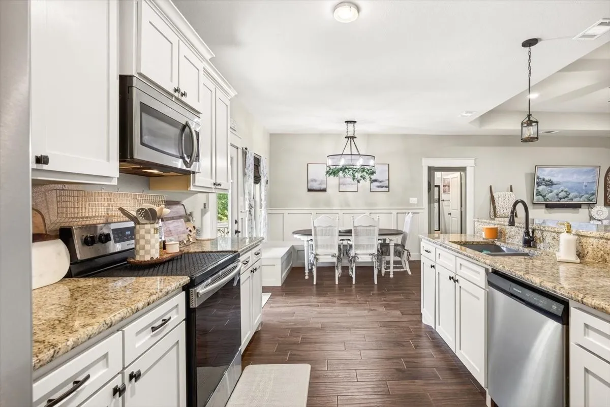 Kitchen featuring white cabinetry, granite countertops, stainless steel appliances, and wood-finish flooring
