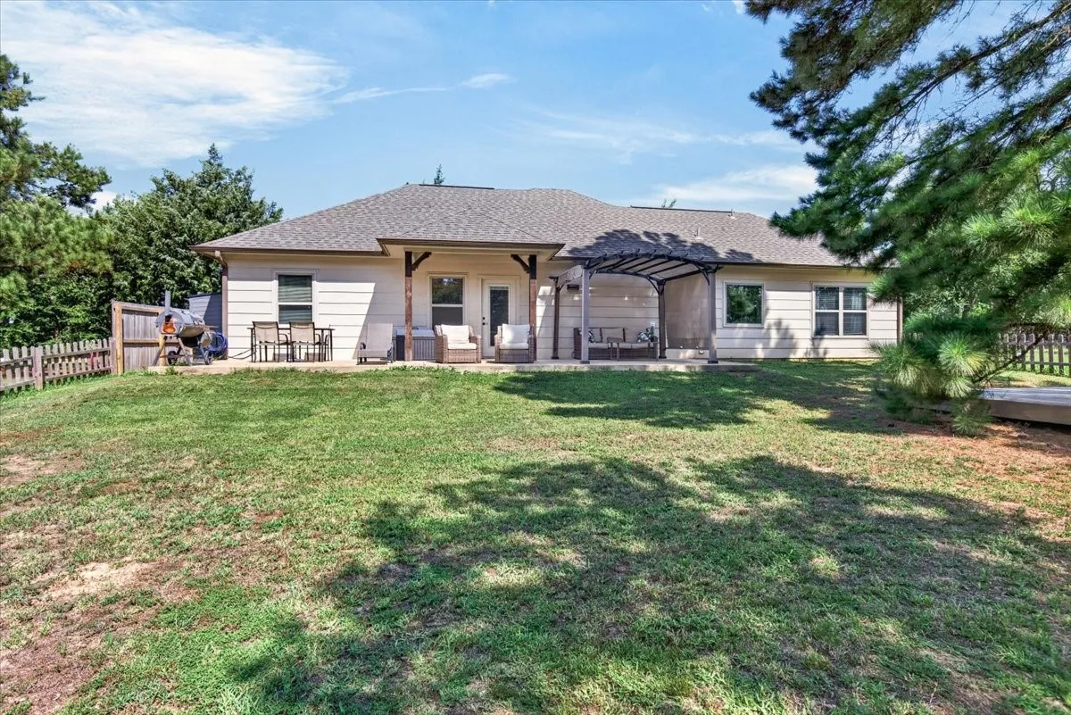 Expansive grassy area with a partial wooden fence, an exterior patio featuring a pergola, and a covered patio with exposed beam supports