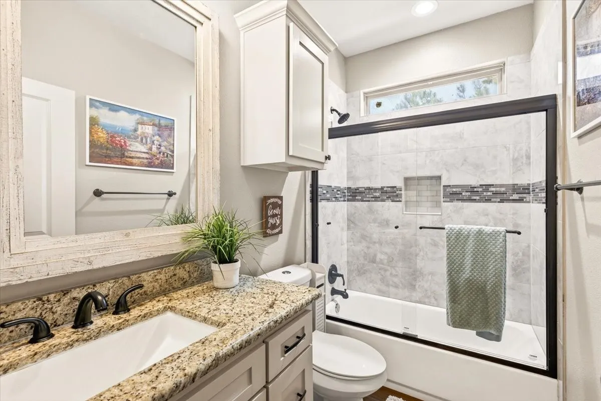 Bathroom featuring a granite vanity, white cabinetry, undermount sink, and a tiled shower-bathtub combination with a glass enclosure