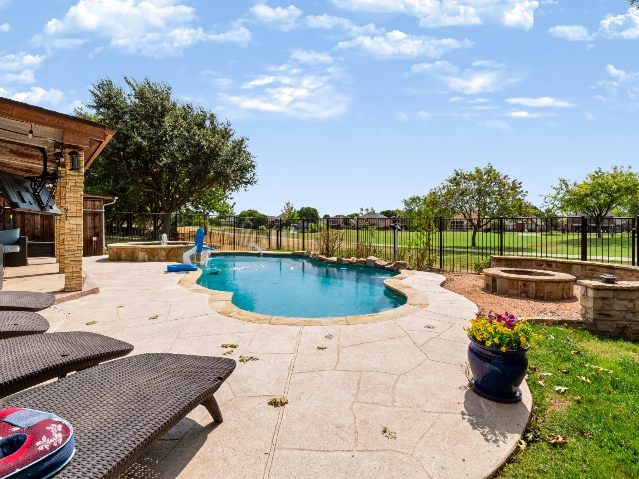 Freeform swimming pool with a rock waterfall feature, an expansive stamped concrete patio, and a stone fire pit on the 16th Hole