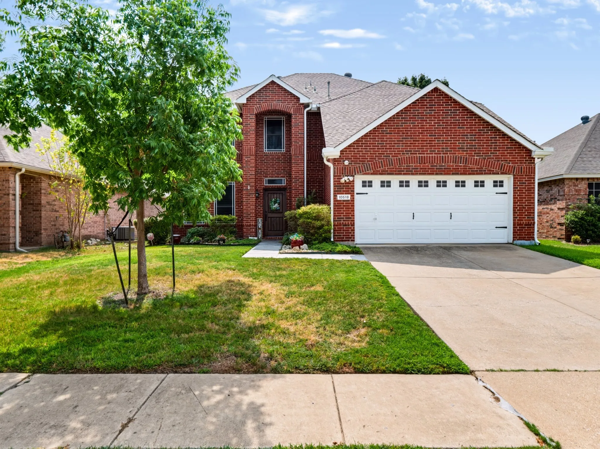 Traditional brick exterior with an attached two-car garage, mature front yard tree, and concrete driveway