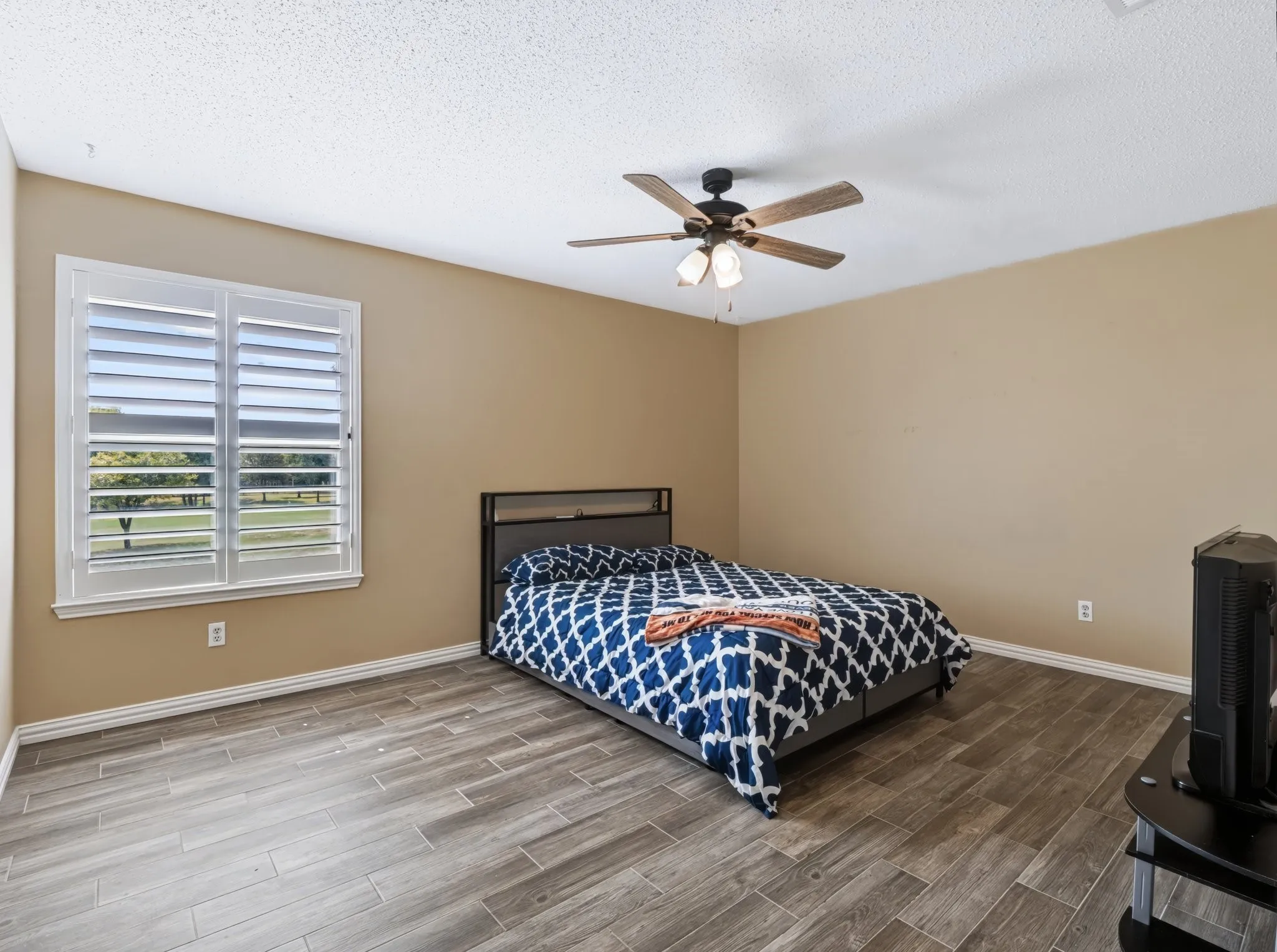 Wood-finish flooring, plantation shutters, and a ceiling fan with integrated lighting