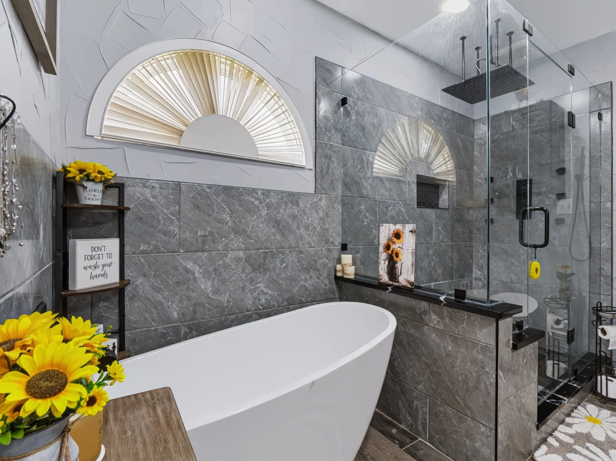 Freestanding soaking tub with a glass-enclosed shower, dark grey wall tiling, and a semicircular transom window
