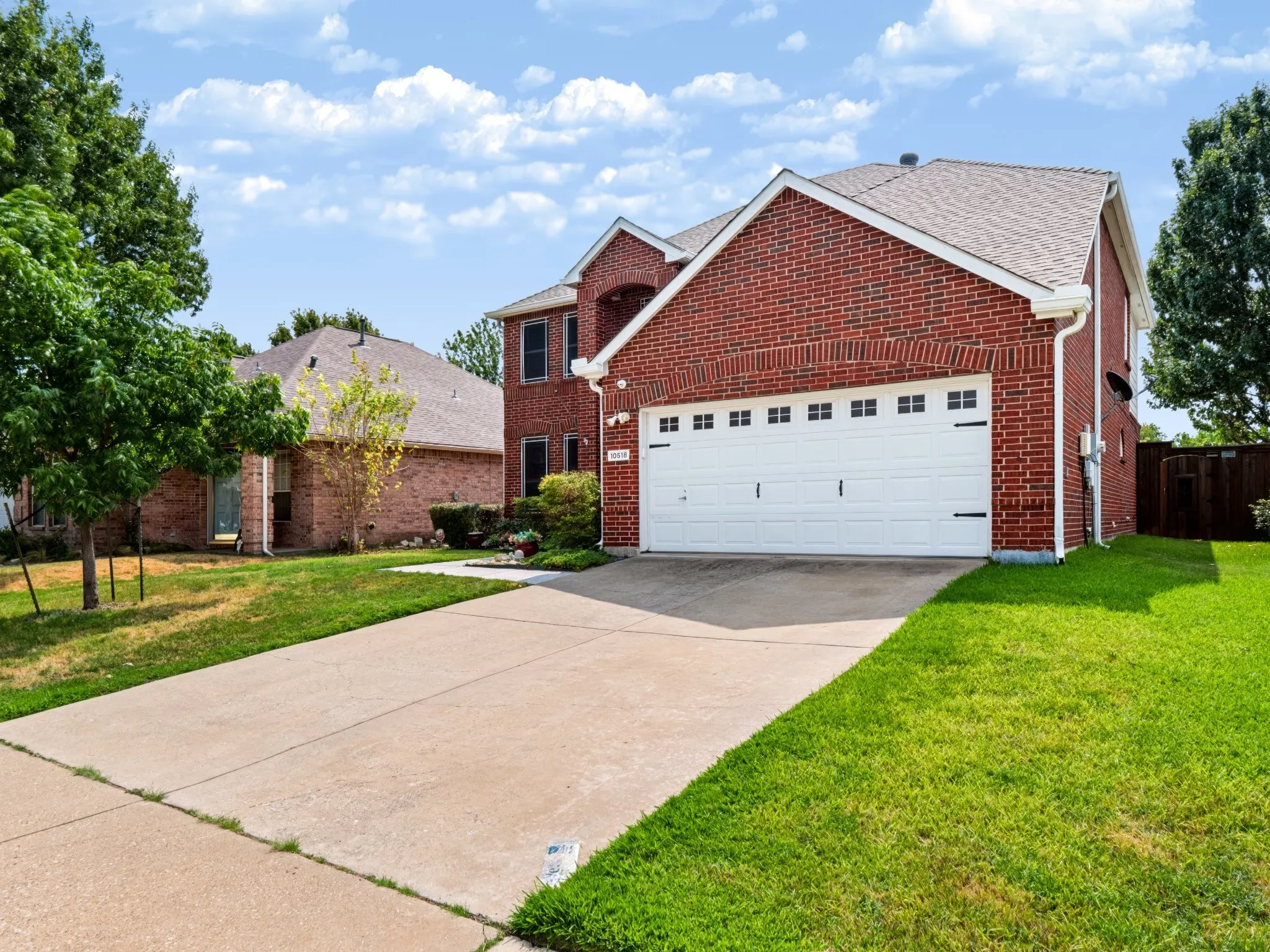 Brick exterior with white garage door, concrete driveway, and established landscaping
