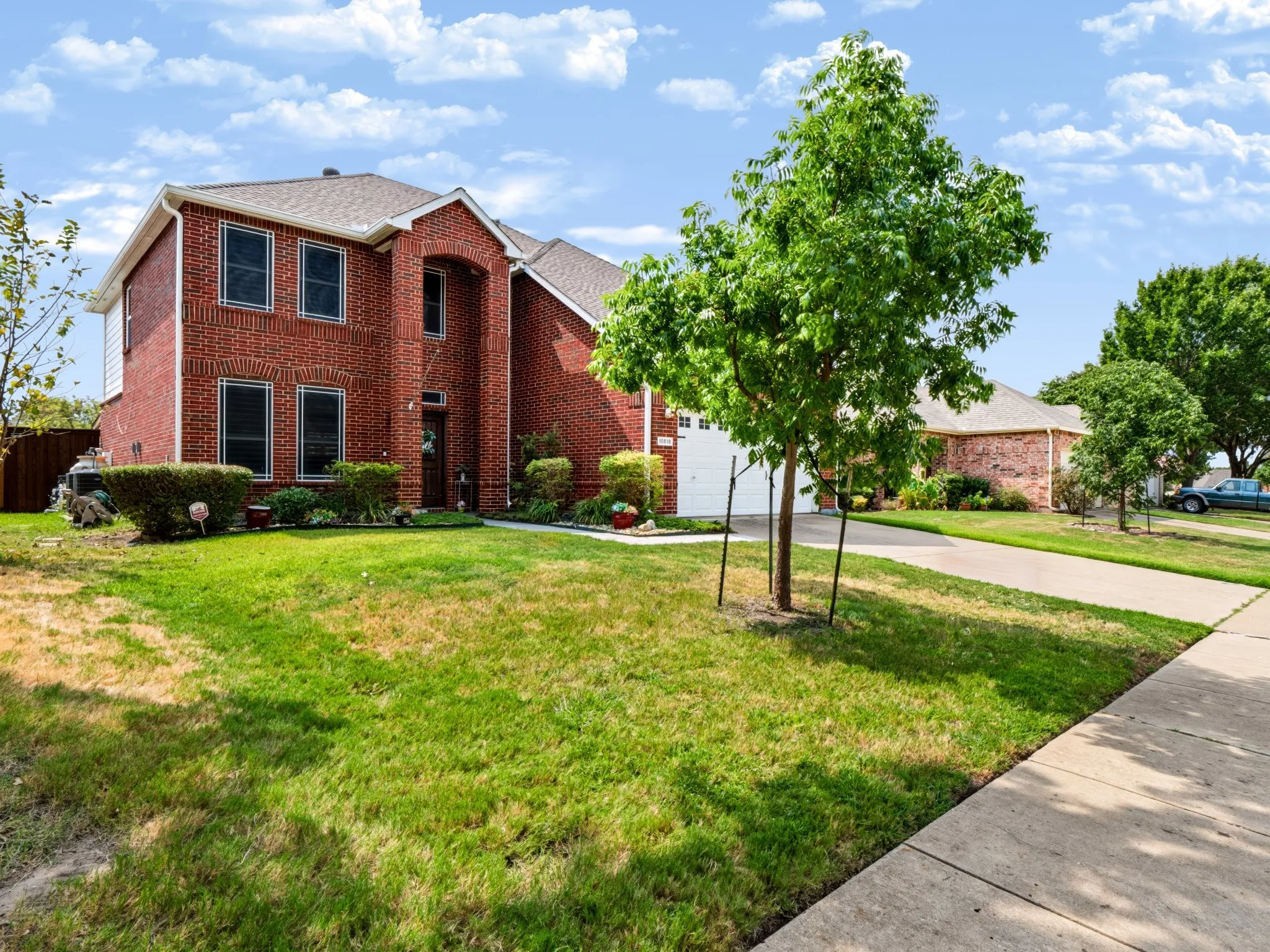 Red brick exterior, two-story architectural design, arched entry detail, concrete driveway, and front lawn