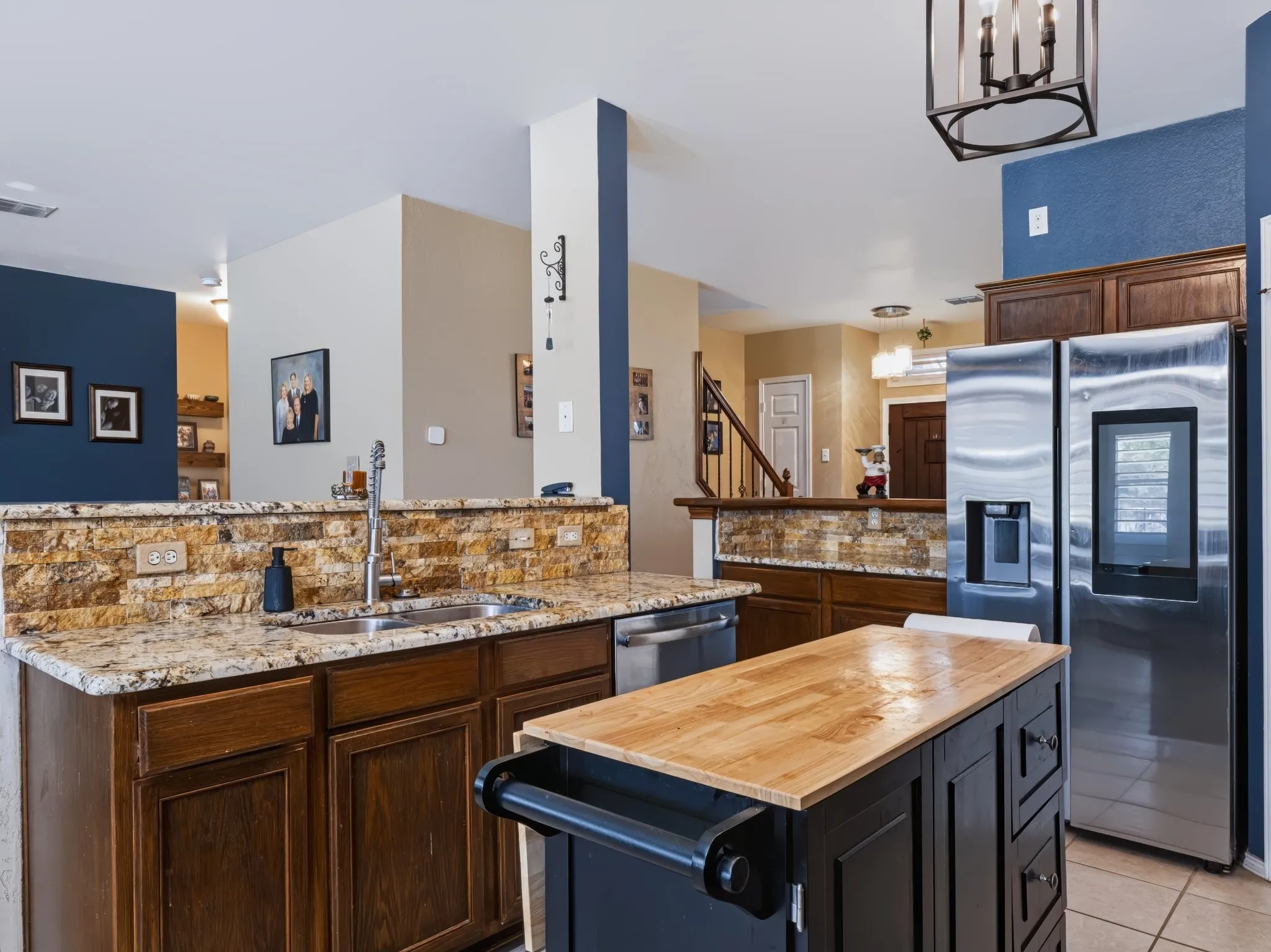 Kitchen featuring granite countertops, a stone tile backsplash, stainless steel appliances, and a mobile kitchen island with a wood-finish top
