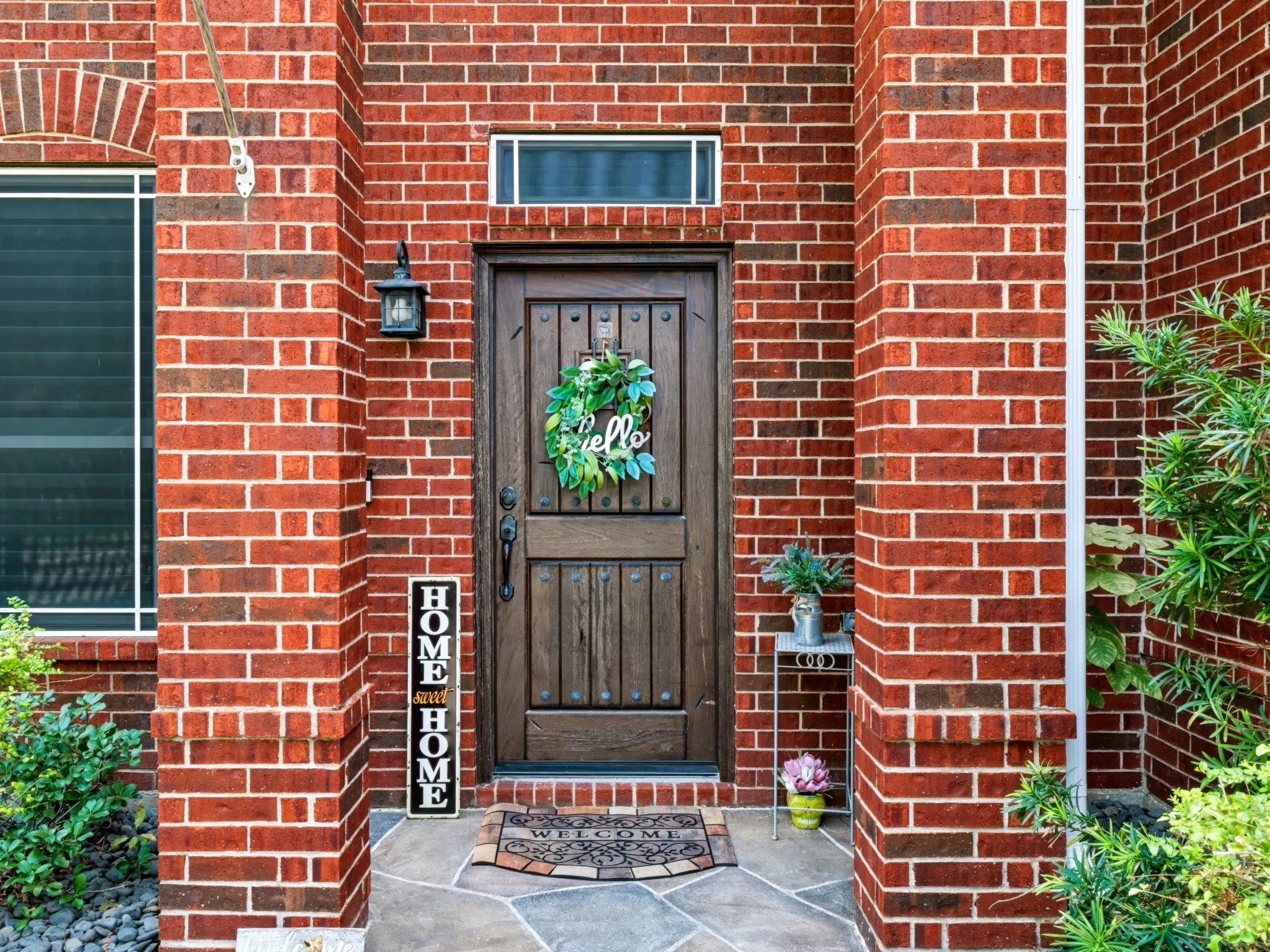 Red brick exterior with a wood-finish entry door, sidelight window, and an exterior wall lantern