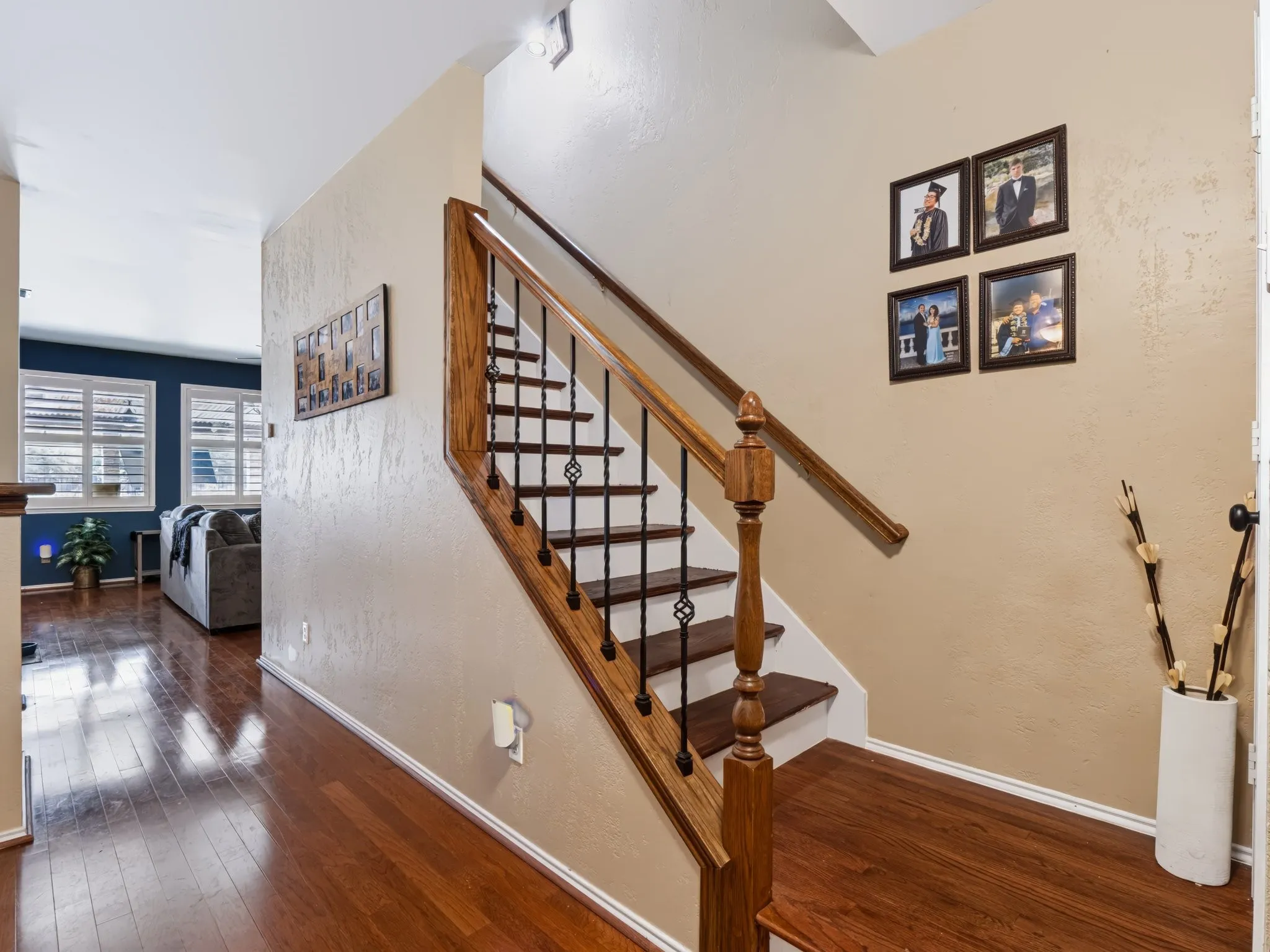 Wood-finish flooring throughout, staircase with wood handrail and wrought iron balusters, white window shutters, and painted interior walls