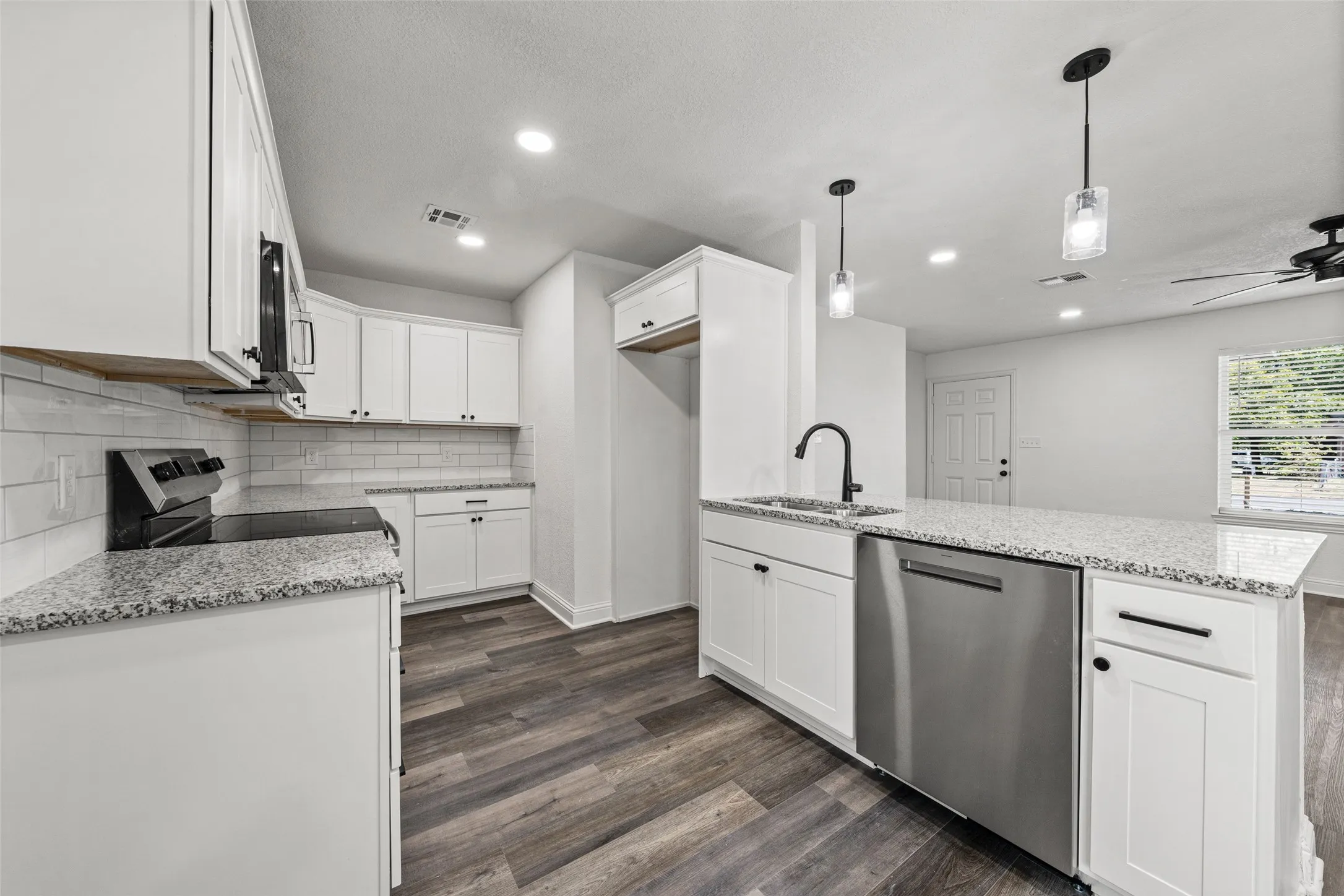 Modern kitchen featuring white cabinetry, stainless steel appliances including a dishwasher, quartz countertops, subway tile backsplash, wood-finish flooring, recessed and pendant lighting, and a center island with prep space
