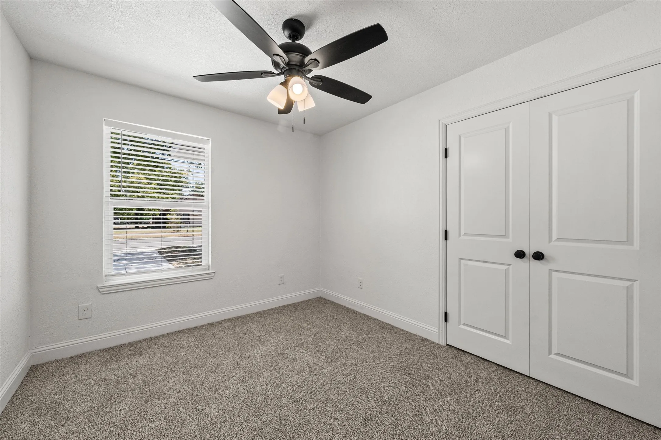 Textured carpet flooring, white painted walls, and white bi-fold doors with black hardware