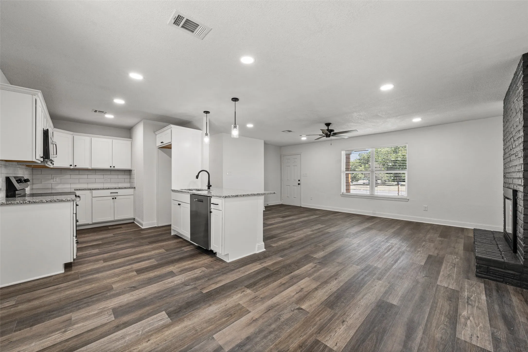 Open-concept living area featuring wood-finish flooring, recessed lighting, and a black brick fireplace