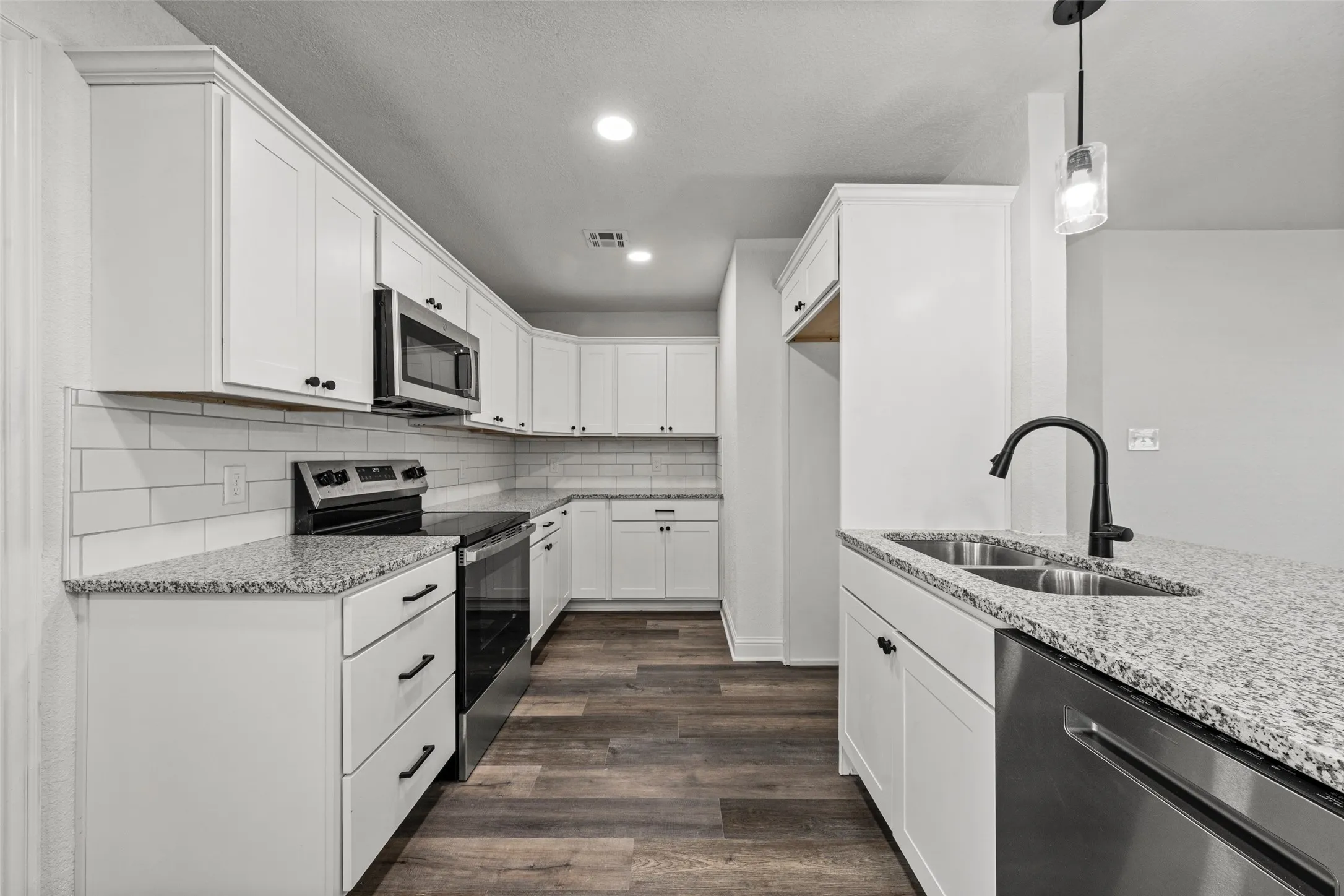 Kitchen featuring white shaker cabinetry, stainless steel appliances, granite countertops, subway tile backsplash, and wood-finish flooring