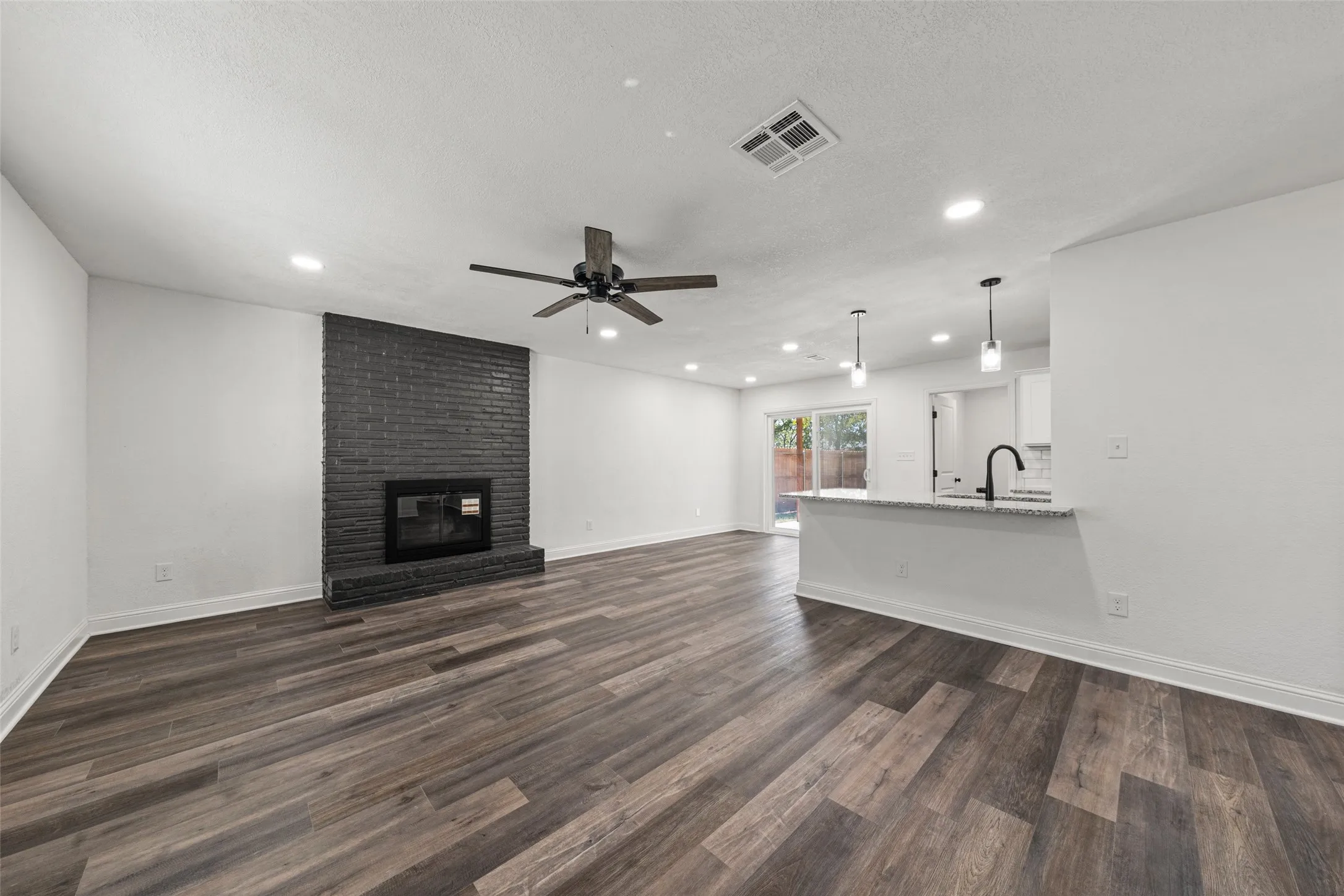 Wood-finish flooring throughout, featuring a dark brick fireplace, recessed lighting, and a ceiling fan