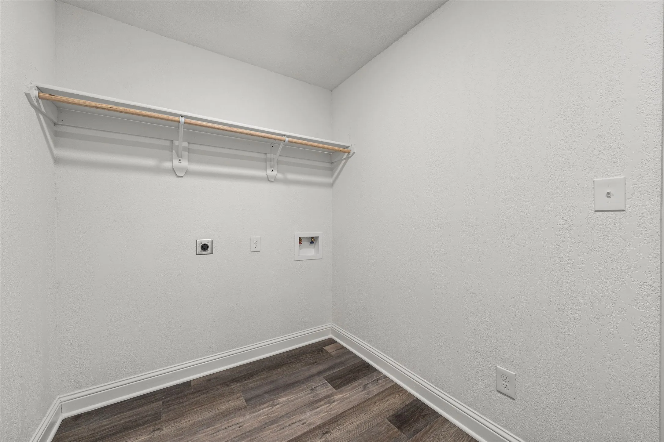 Laundry area featuring wood-finish flooring, a wall-mounted clothing rod, and appliance hookups