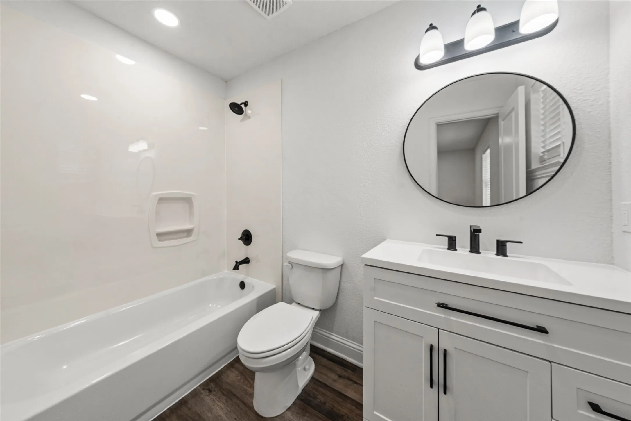White vanity with a single basin sink, matte black faucet, and oval mirror, complemented by wood-finish flooring
