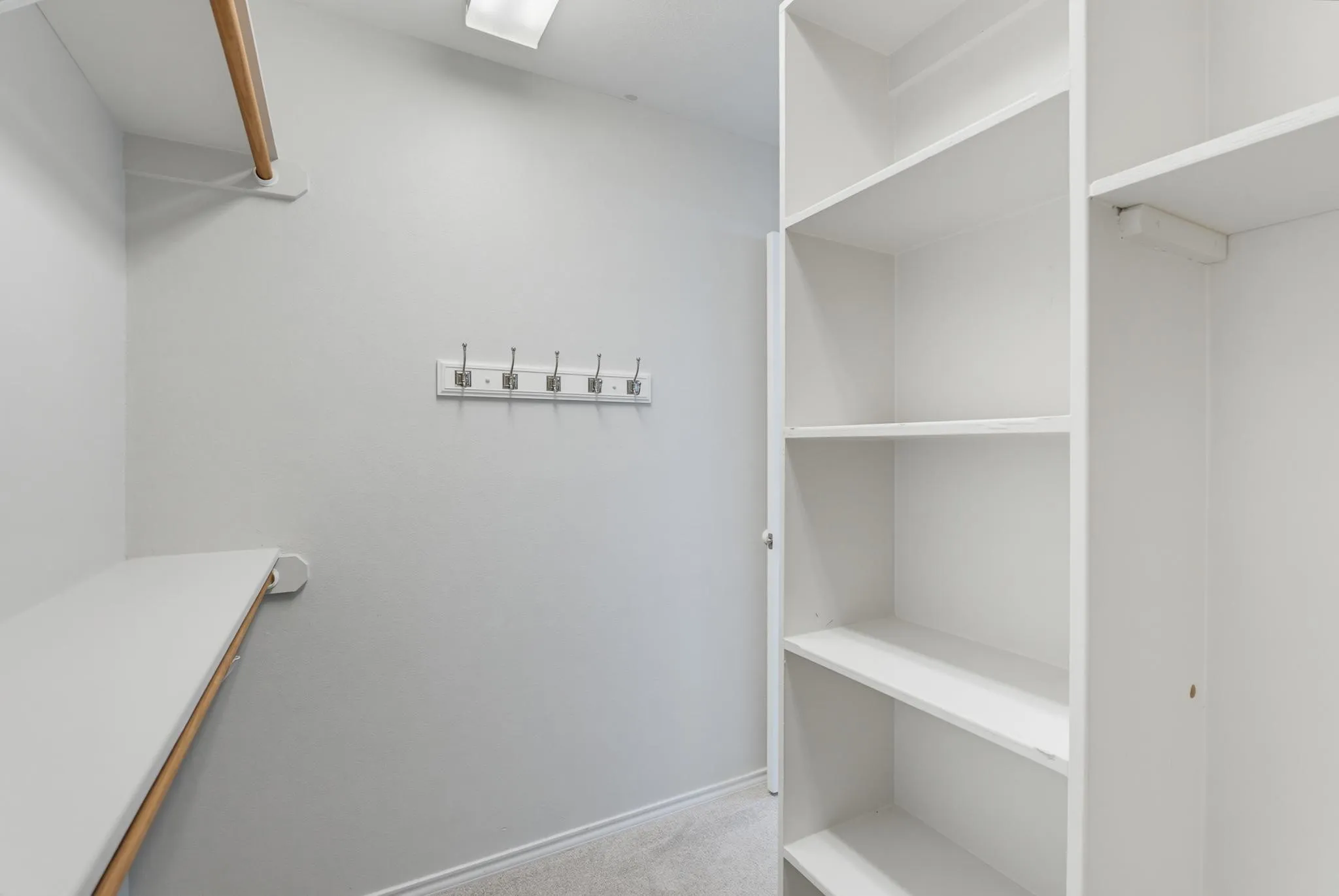 Spacious walk-in closet featuring built-in shelving with multiple compartments, a wooden-finish hanging rod, and recessed ceiling lighting