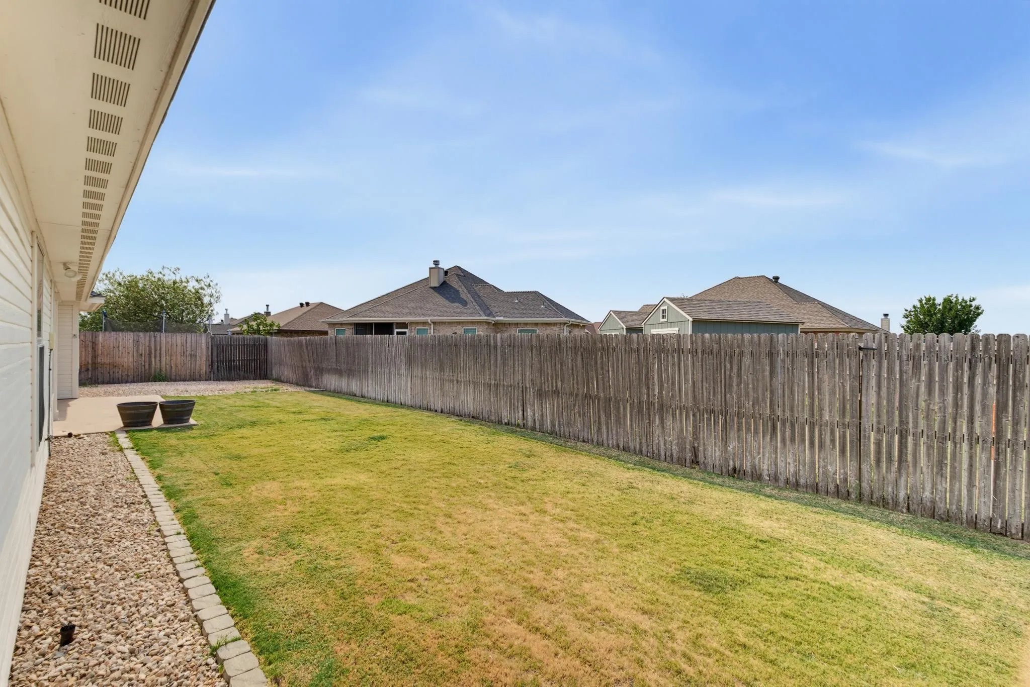Expansive backyard featuring a wood privacy fence, a concrete patio, and a gravel-lined border