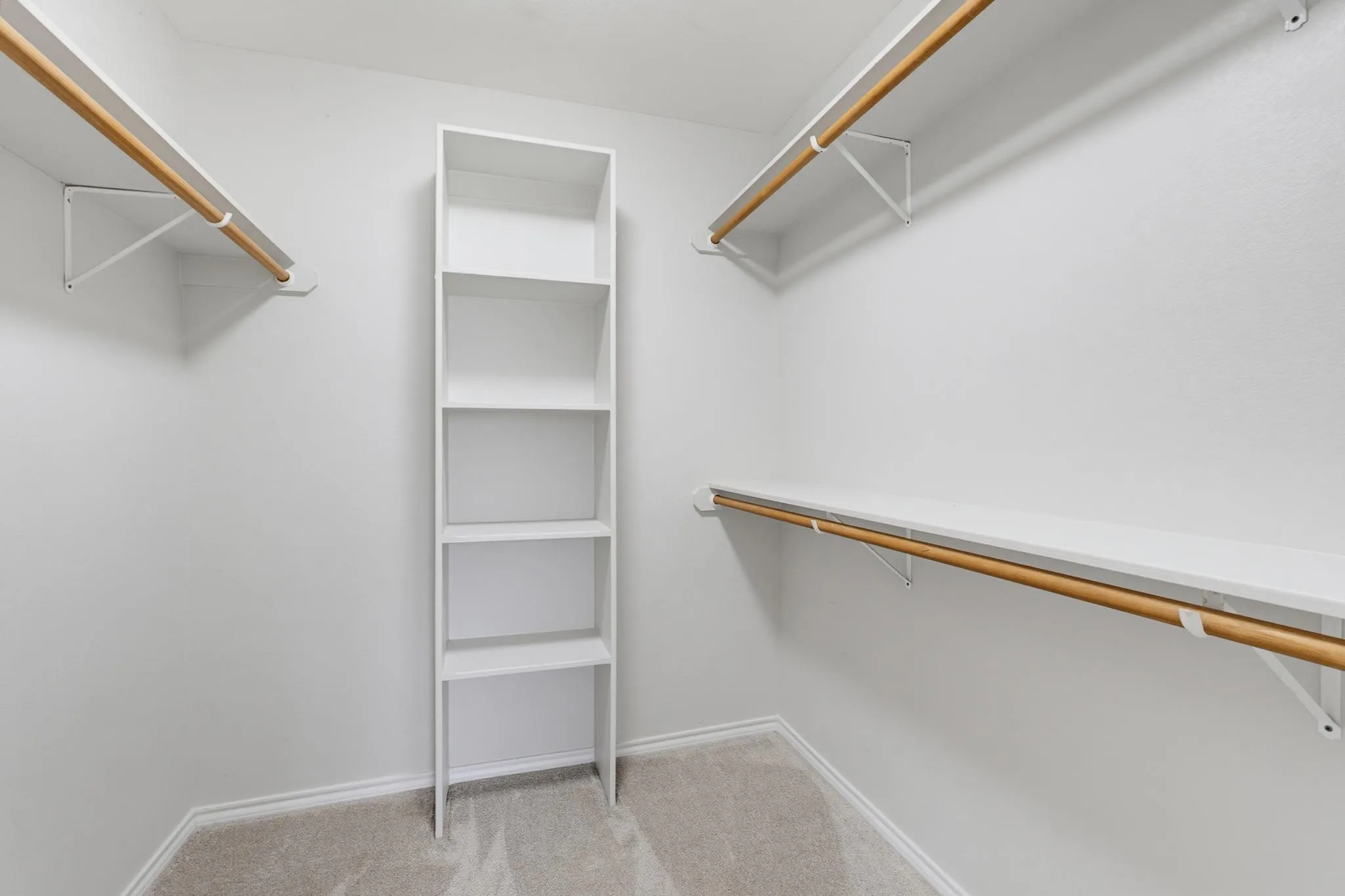 Walk-in closet featuring light-colored carpeting, multiple hanging rods, and integrated shelving