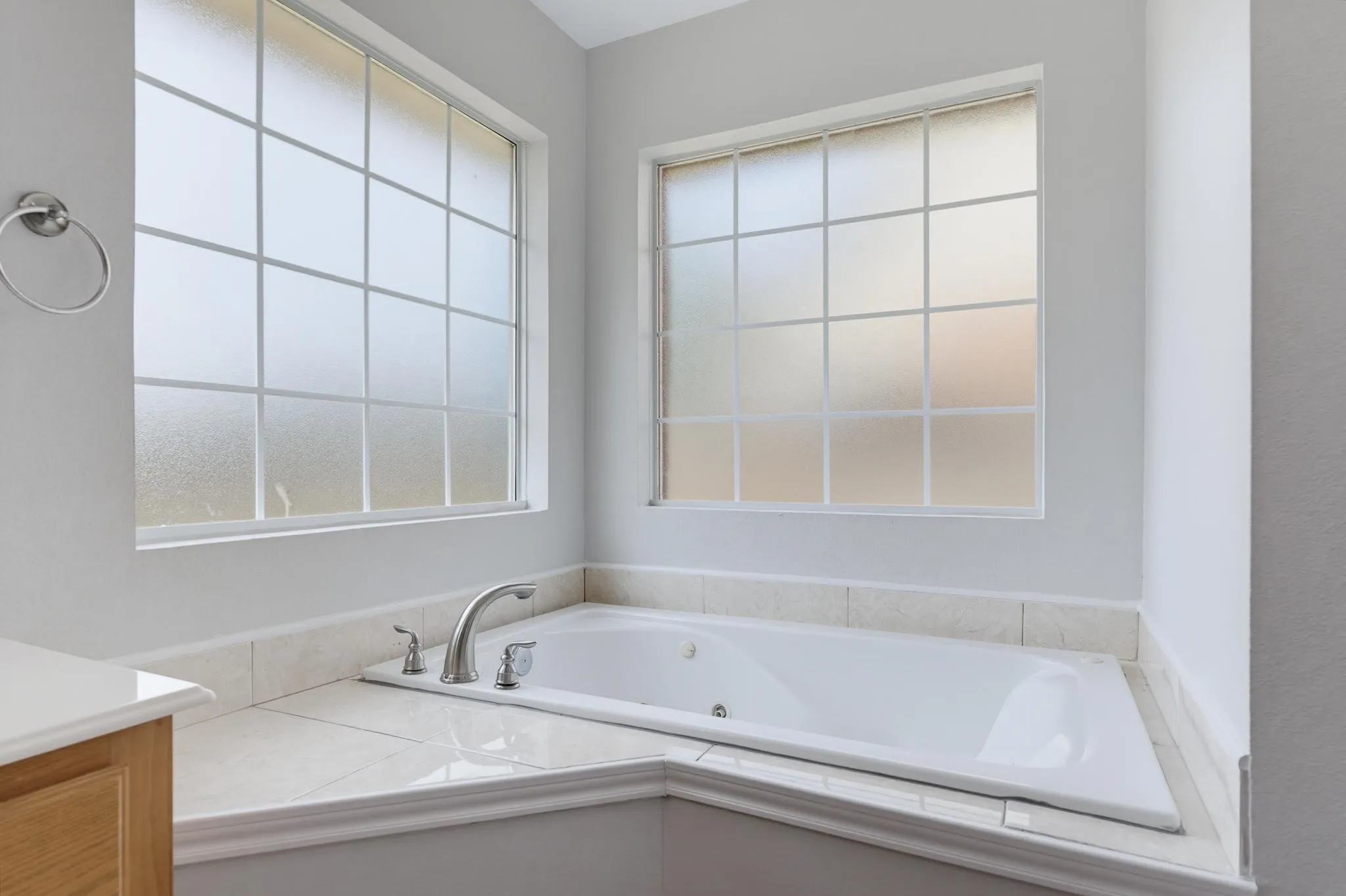 Built-in jetted tub surrounded by tile, brushed nickel fixtures, and privacy glass windows