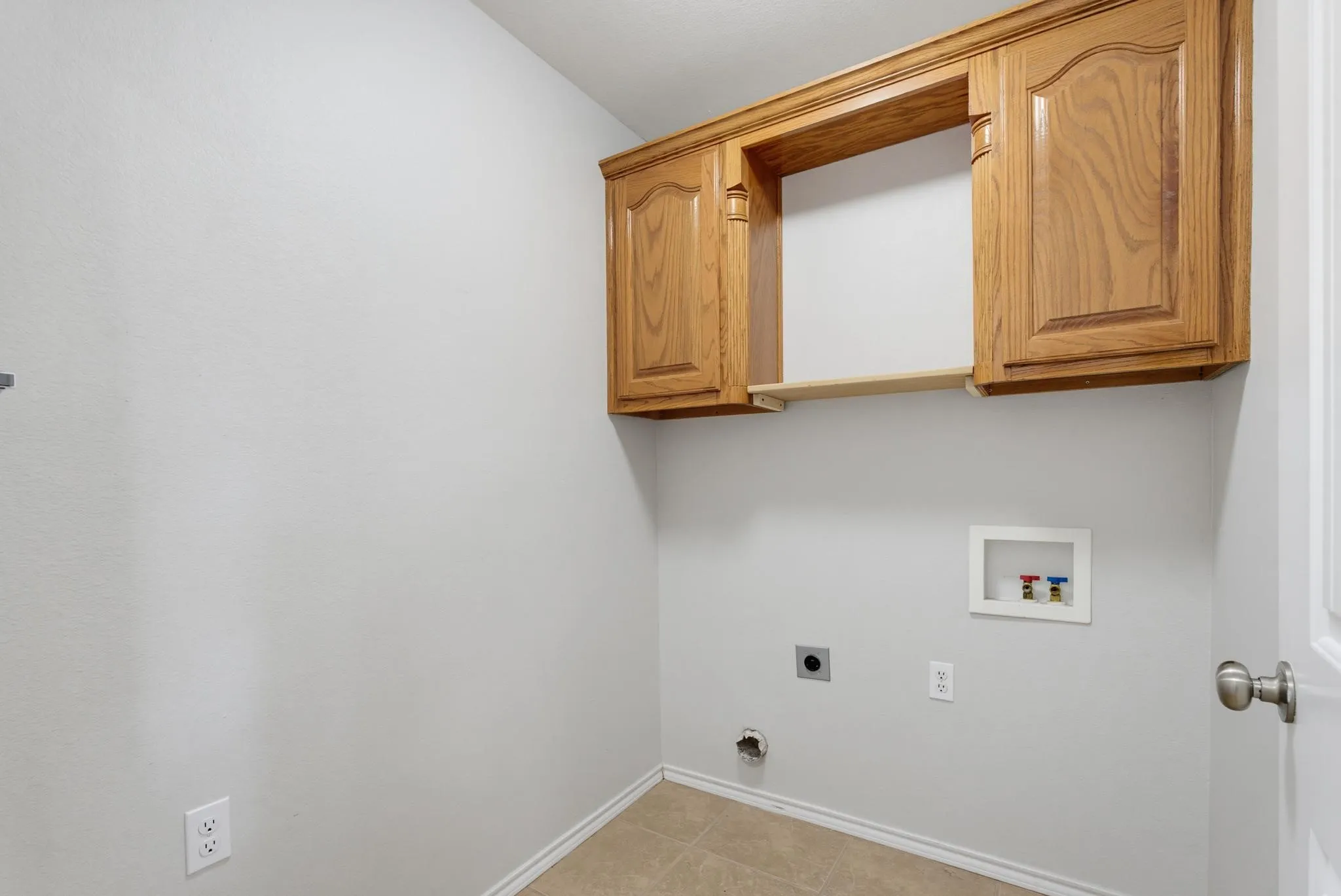 Utility room featuring wood-finish cabinetry with ample storage, neutral wall finishes, and multiple electrical outlets for appliance connections