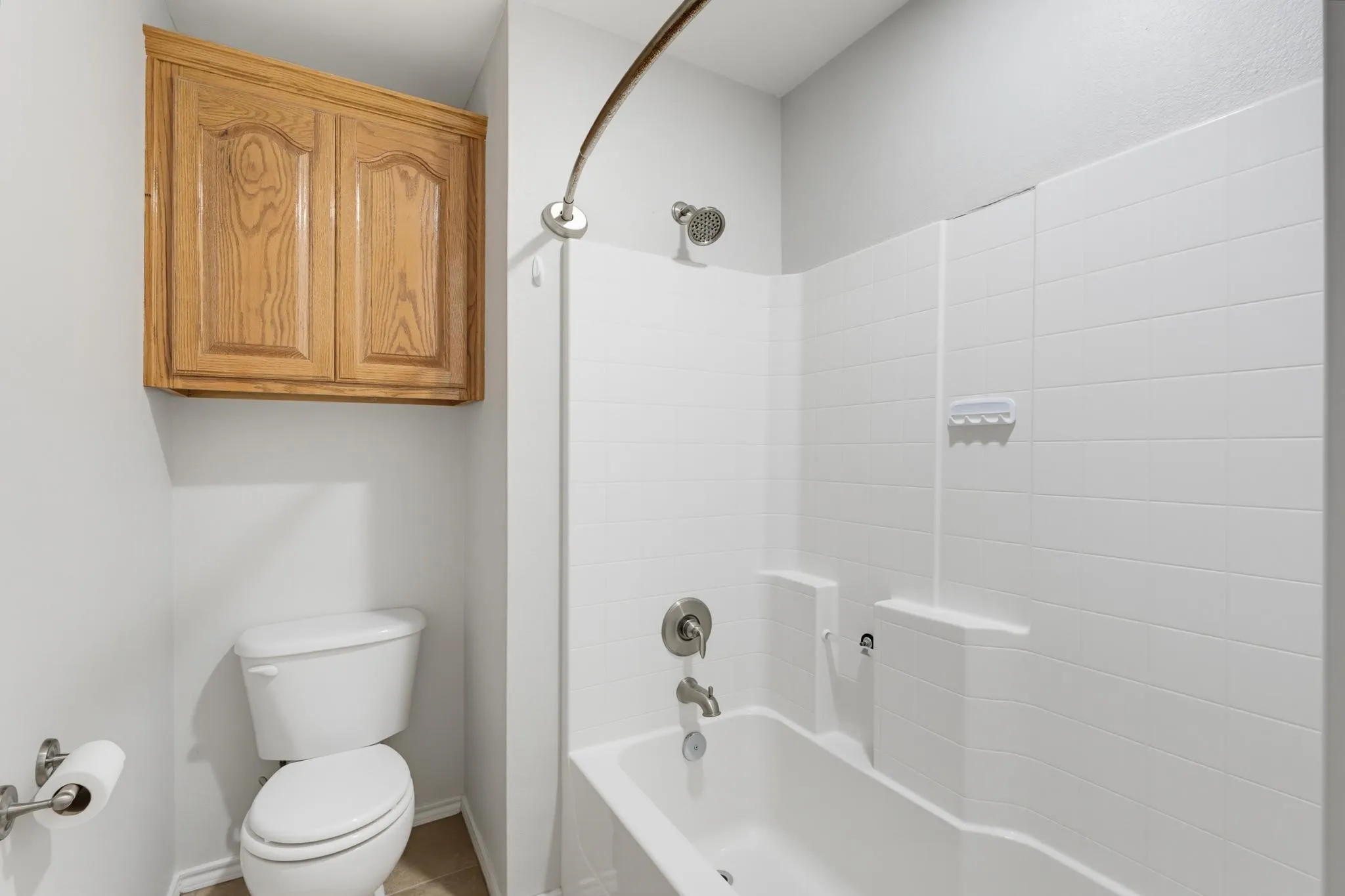 Clean and functional bathroom featuring white subway tile surround, an integrated bathtub and shower combination with chrome fixtures, a wood-finish vanity cabinet with storage, and a separate toilet area with chrome hardware