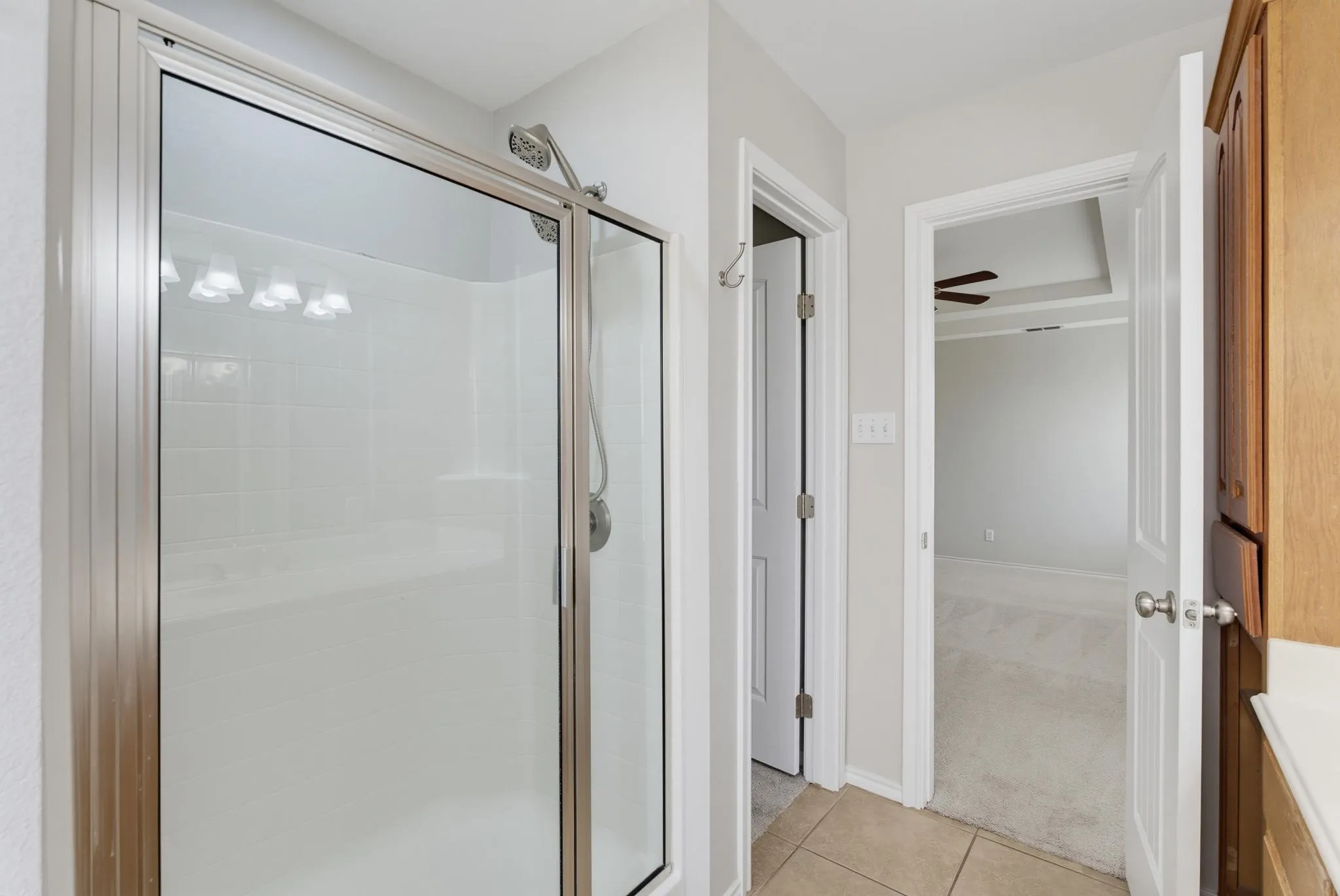 Primary Bathroom featuring a frameless glass-enclosed shower with brushed nickel fixtures, ceramic tile surround, and neutral stone-finish flooring